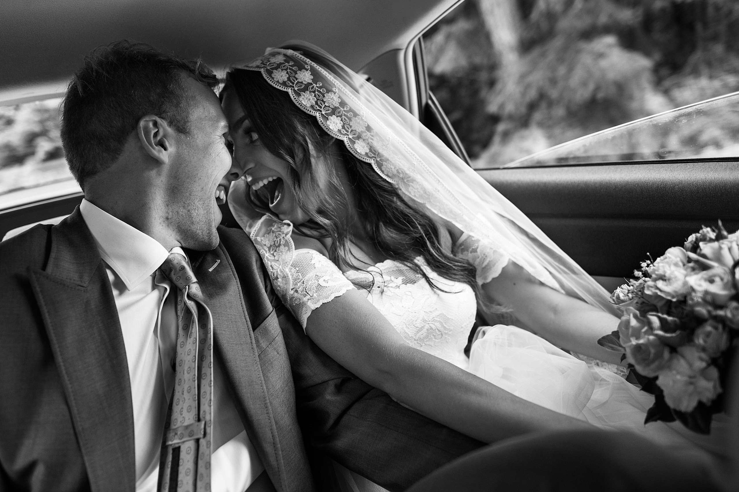 A bride and groom sitting in the back seat of a car with big smiles - Qualicum Wedding Photographer