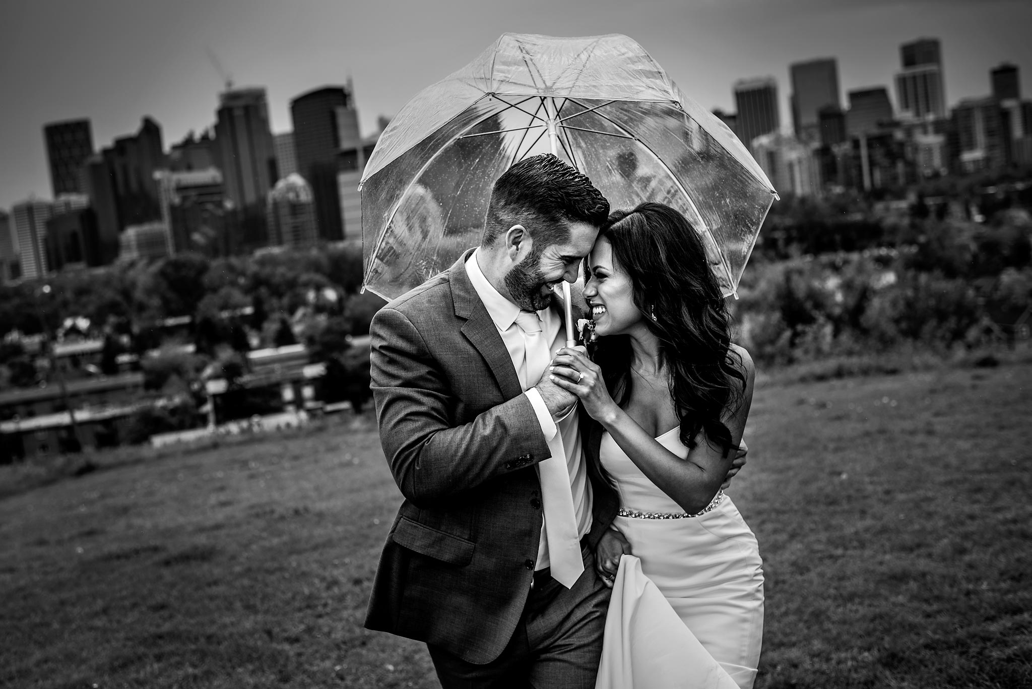 bride and groom walking up a hill together holding an umbrella with the downtown city skyline in the background - calgary sean leblanc wedding photographers