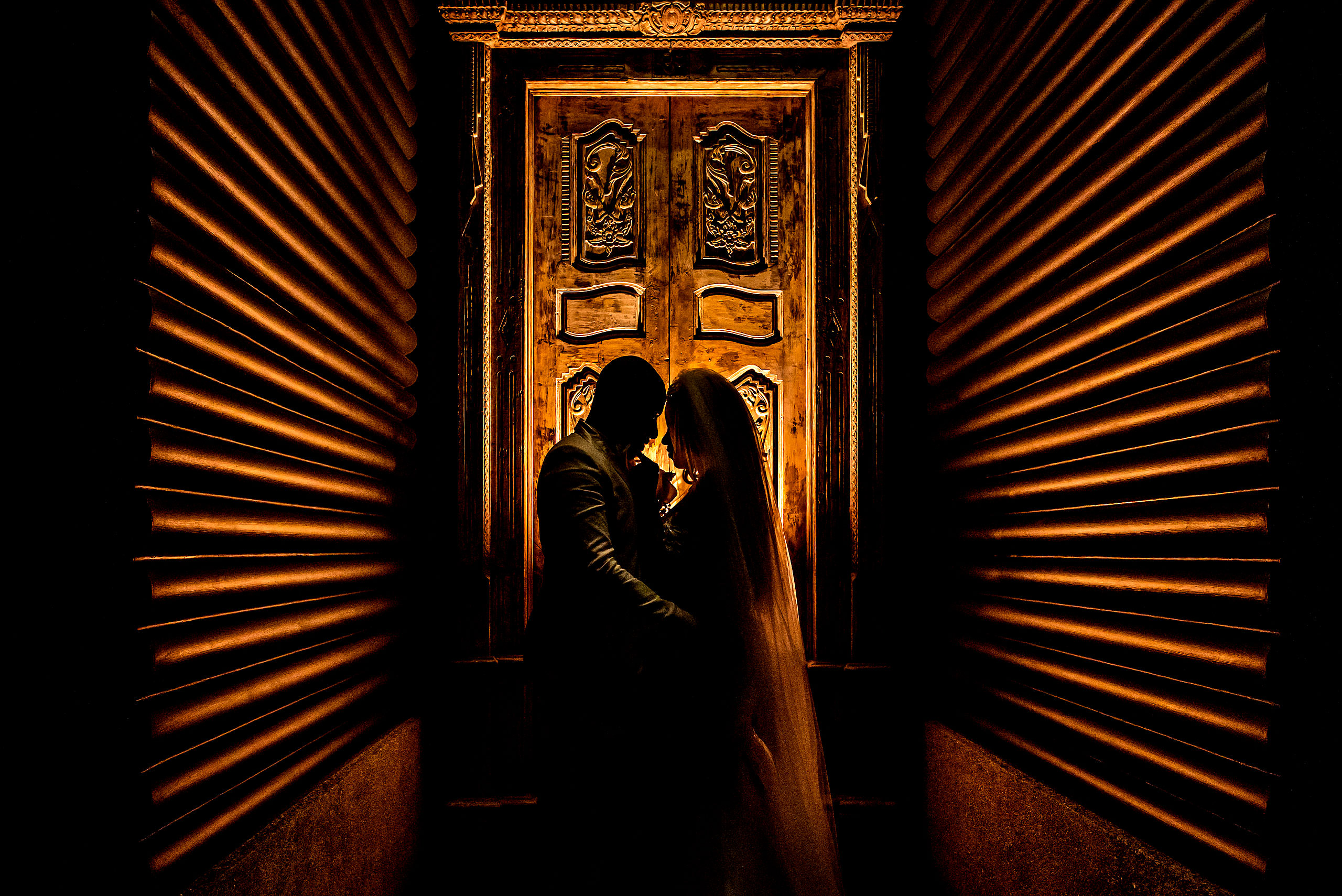 bride and groom embracing silhouetted against a carved door by calgary sean leblanc wedding photographers