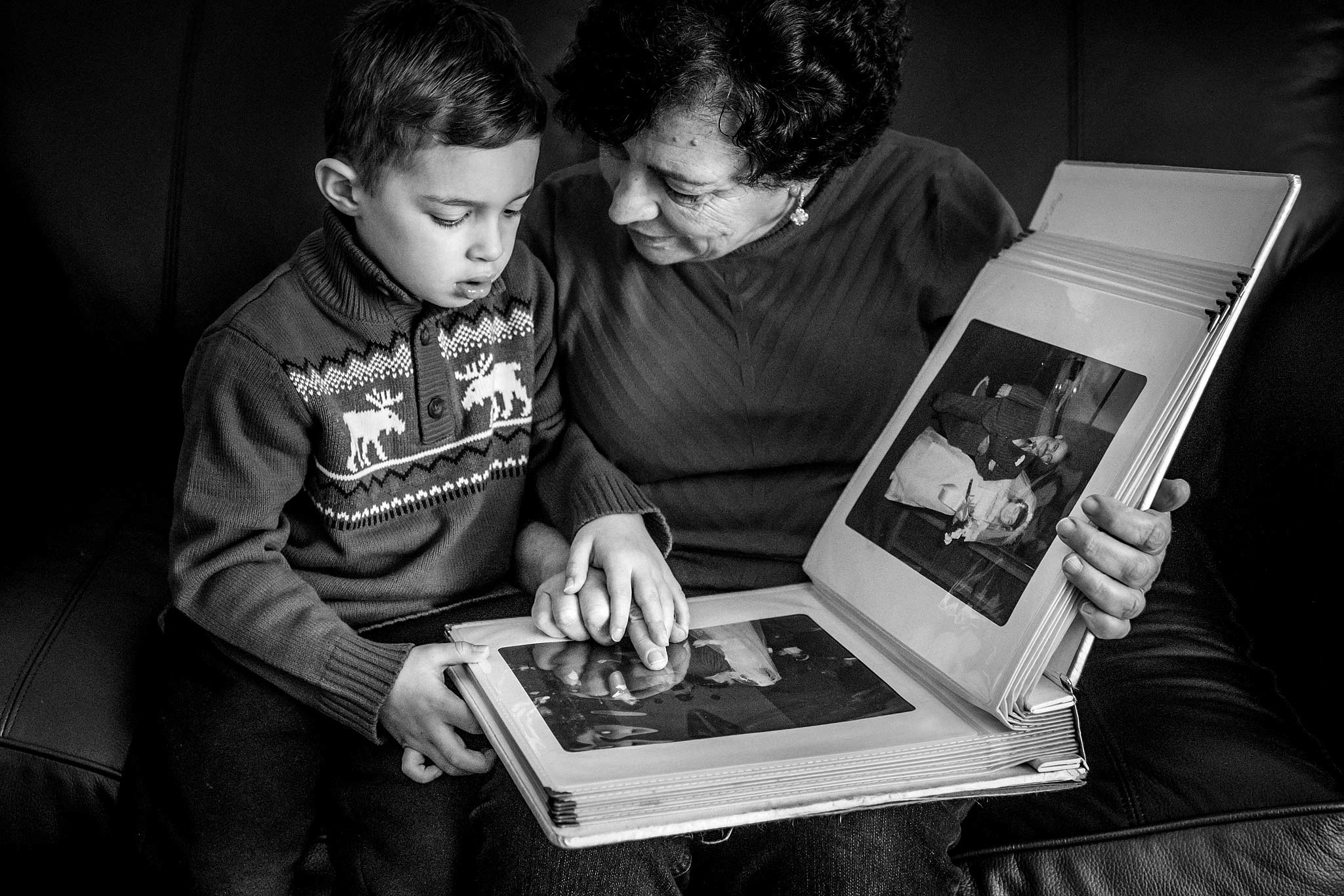 Grandma and boy looking through her old wedding album while sitting on a sofa top wedding photographer sean leblanc