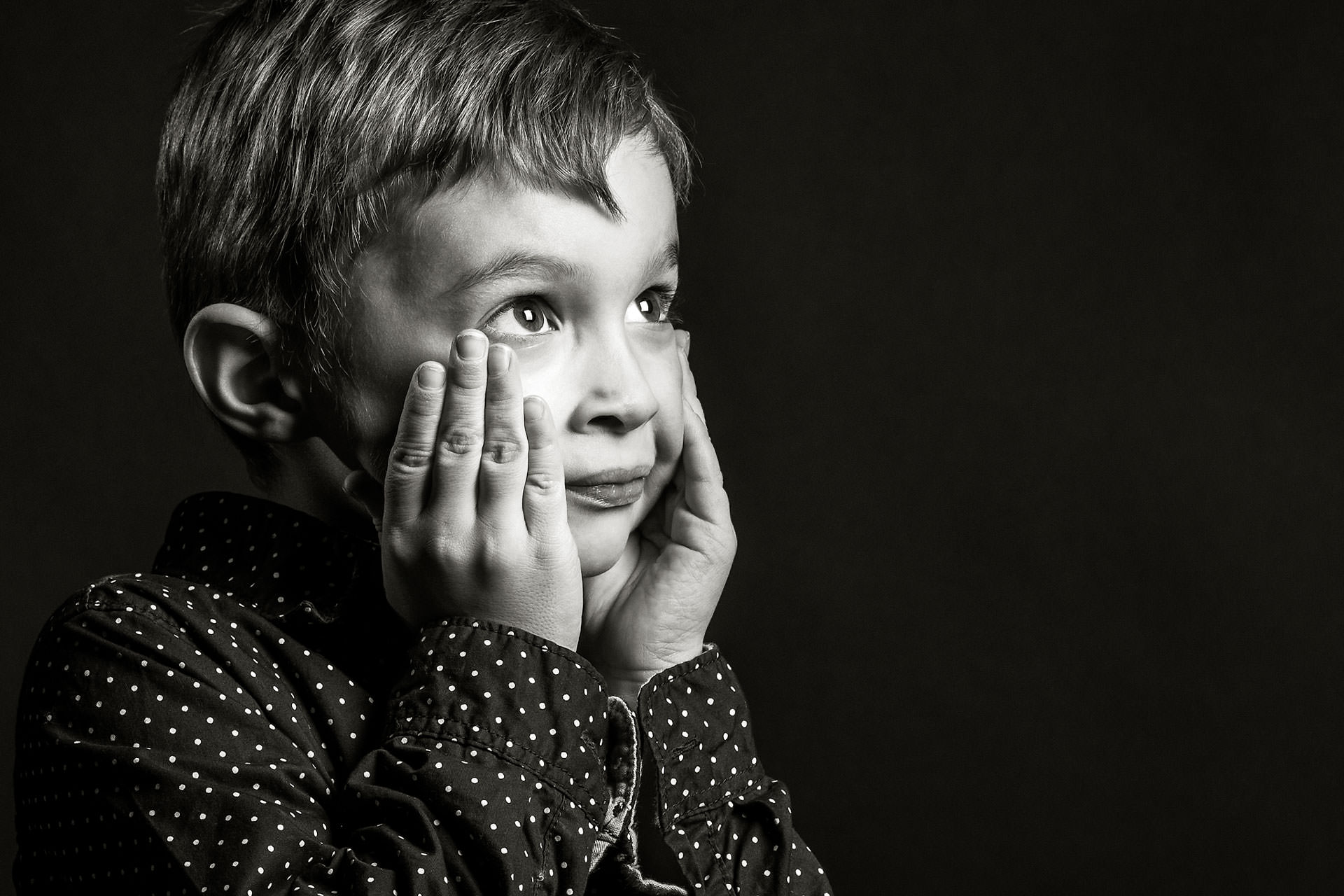 a young boy with his hands on either side of his face looking upward against a black backdrop by top family portrait photographer sean leblanc