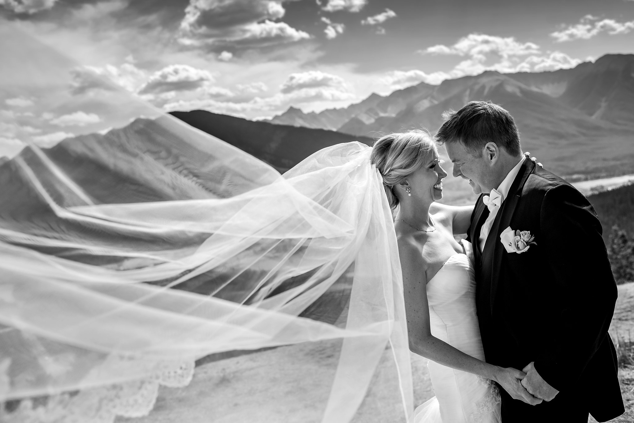 bride and groom smiling at each other with her veil flowing in the wind by calgary wedding photographer sean leblanc