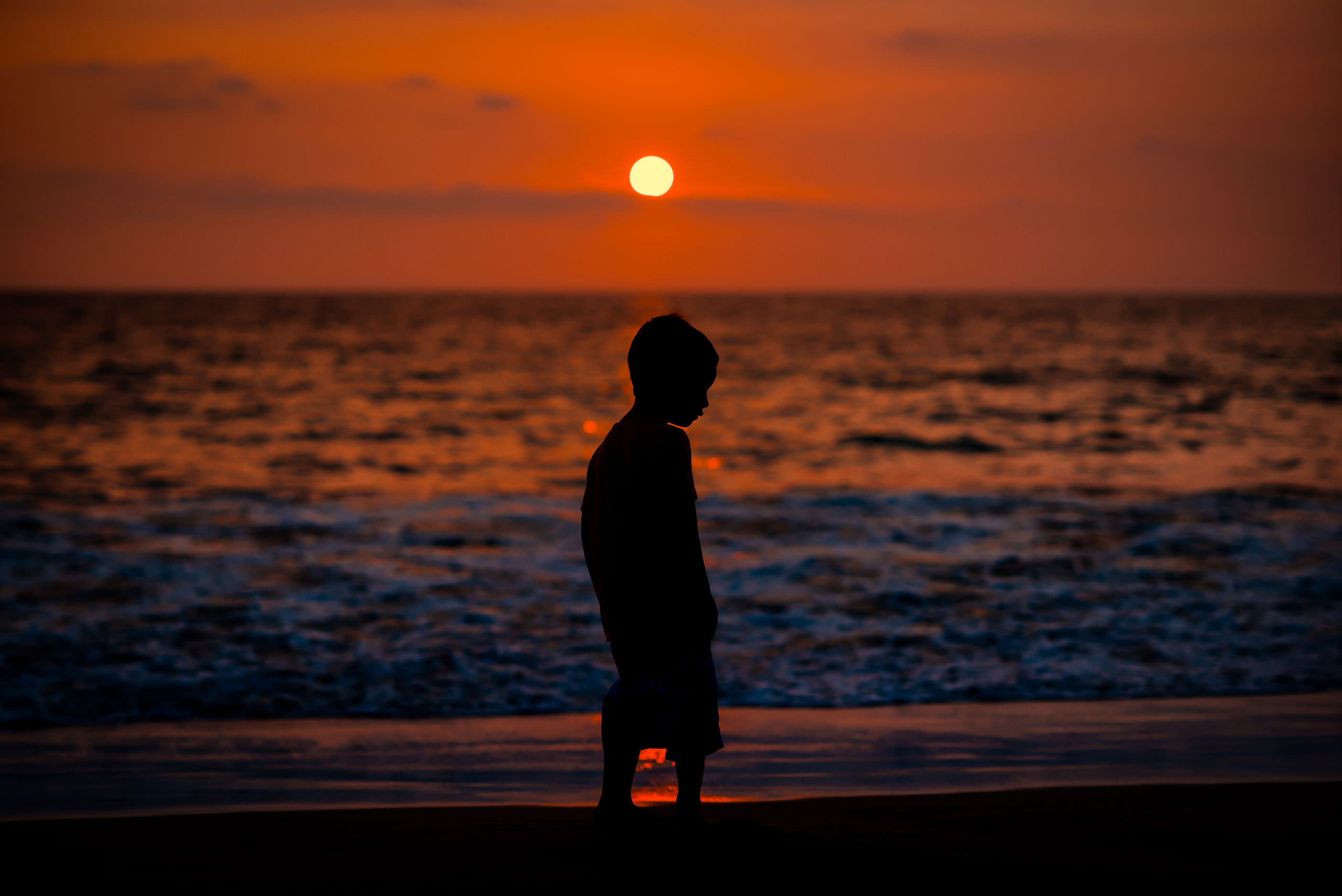 young boy on a Hawaiian beach at sunset silhouetted against the ocean by destination family photographers sean leblanc