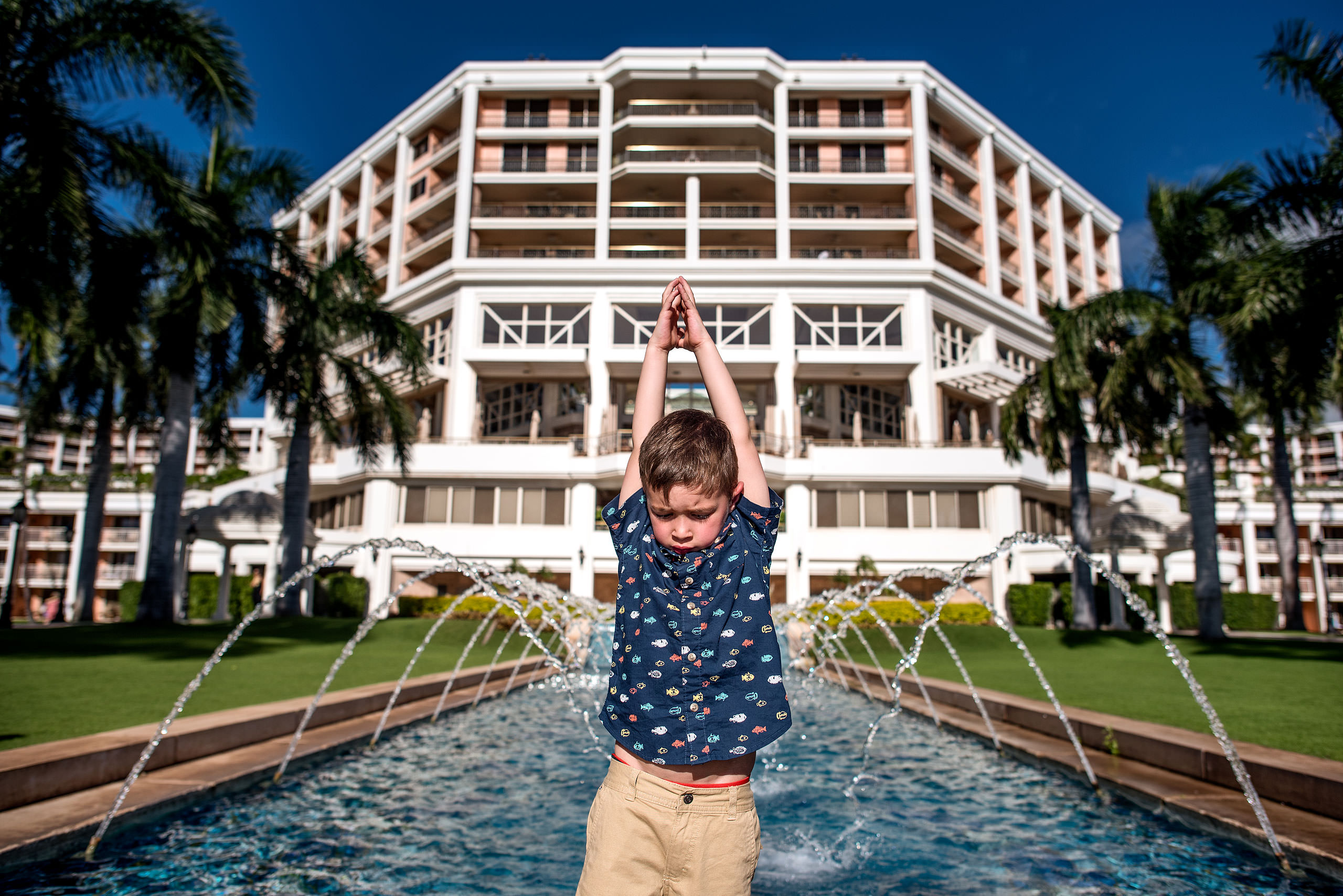 a young boy raising his arms in front of a hotel in Hawaii by destination family photographers sean leblanc