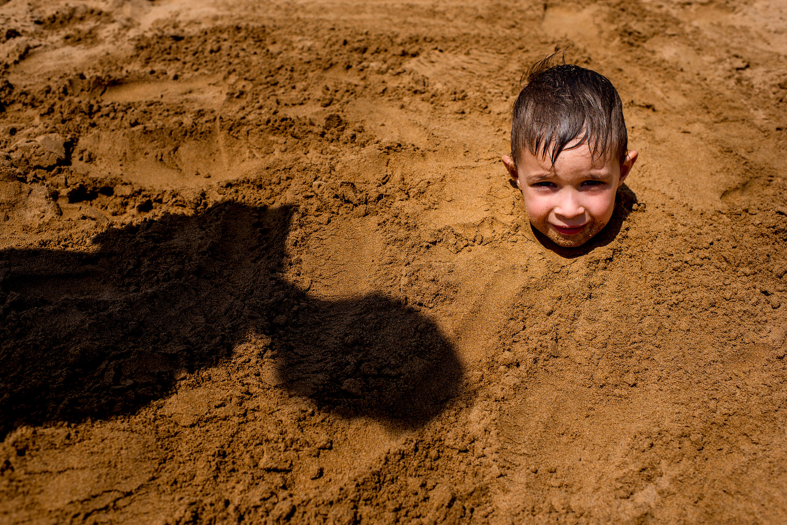 a young boy buried in the sand up to his neck by destination family photographers sean leblanc