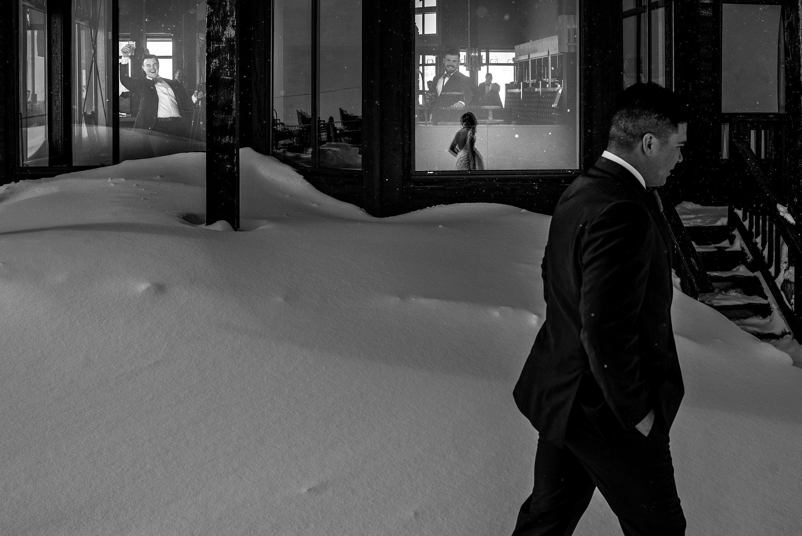 groom walking past a building at winter kicking horse wedding