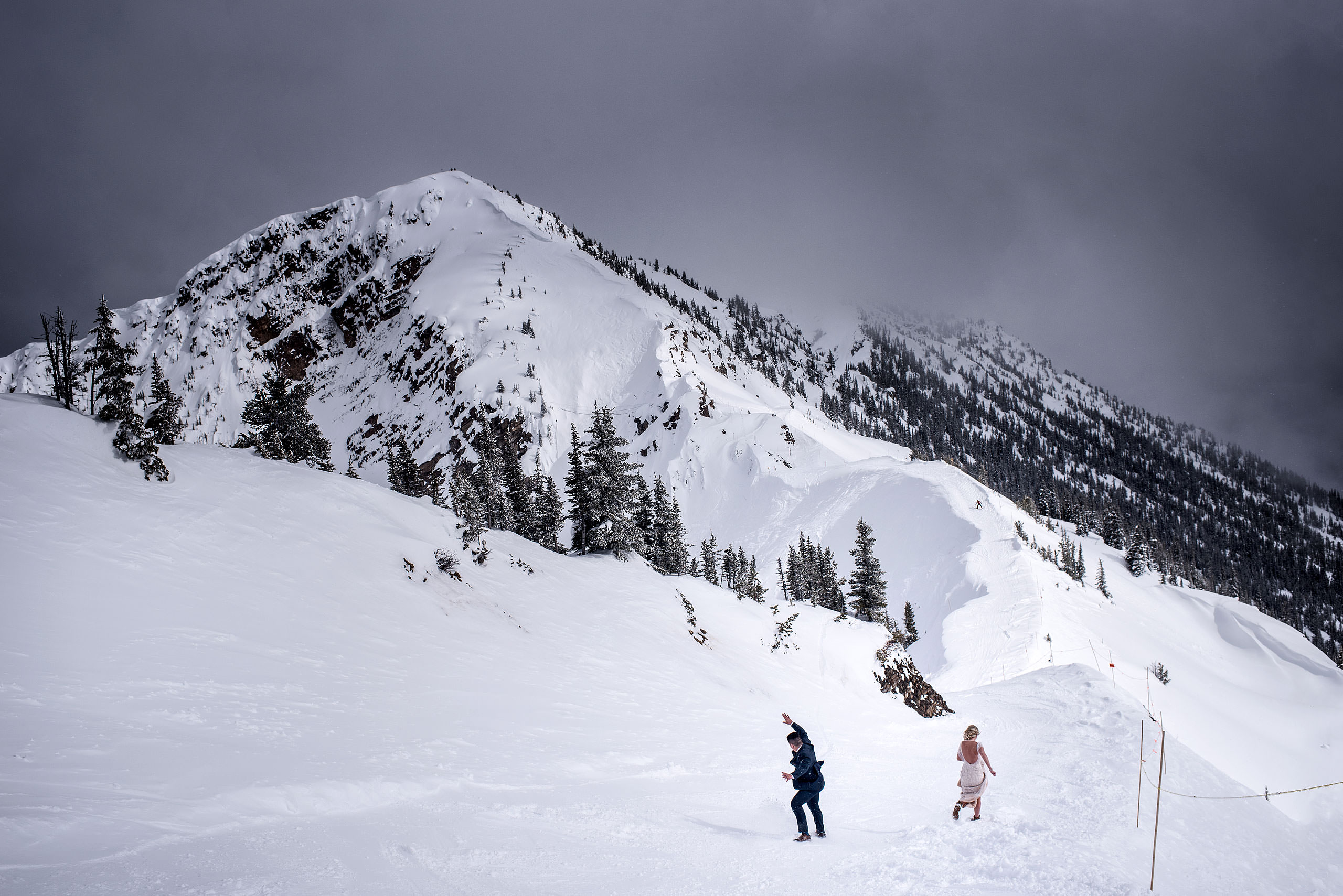 a bride and groom sliding down the side of a mountain at a winter kicking horse wedding by sean leblanc