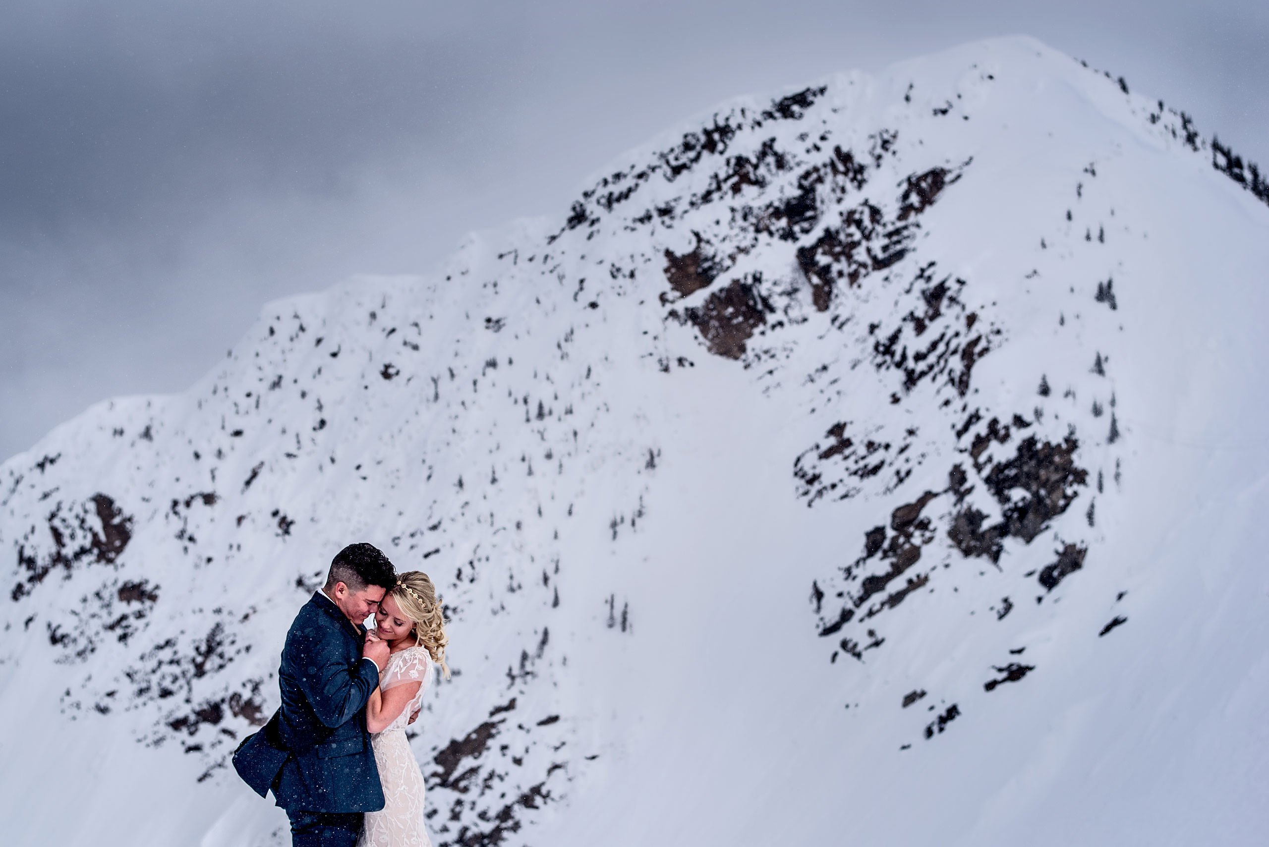 a bride and groom embracing each other in front of a mountain at a winter kicking horse wedding by sean leblanc