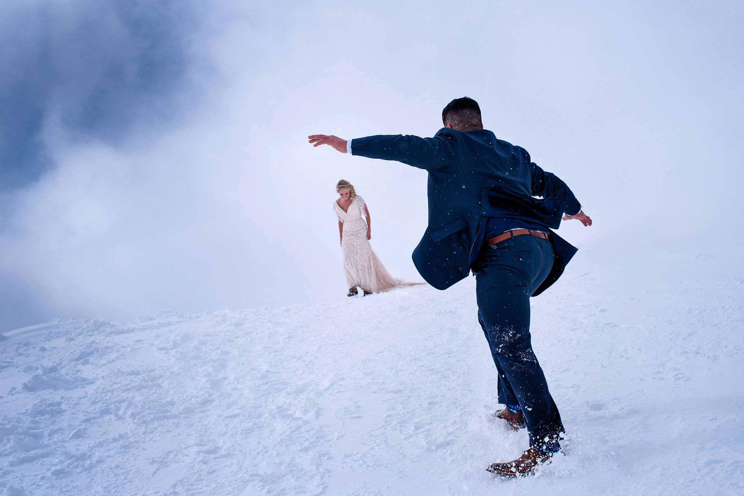 a groom sliding down a snowy hill at a winter kicking horse wedding by sean leblanc