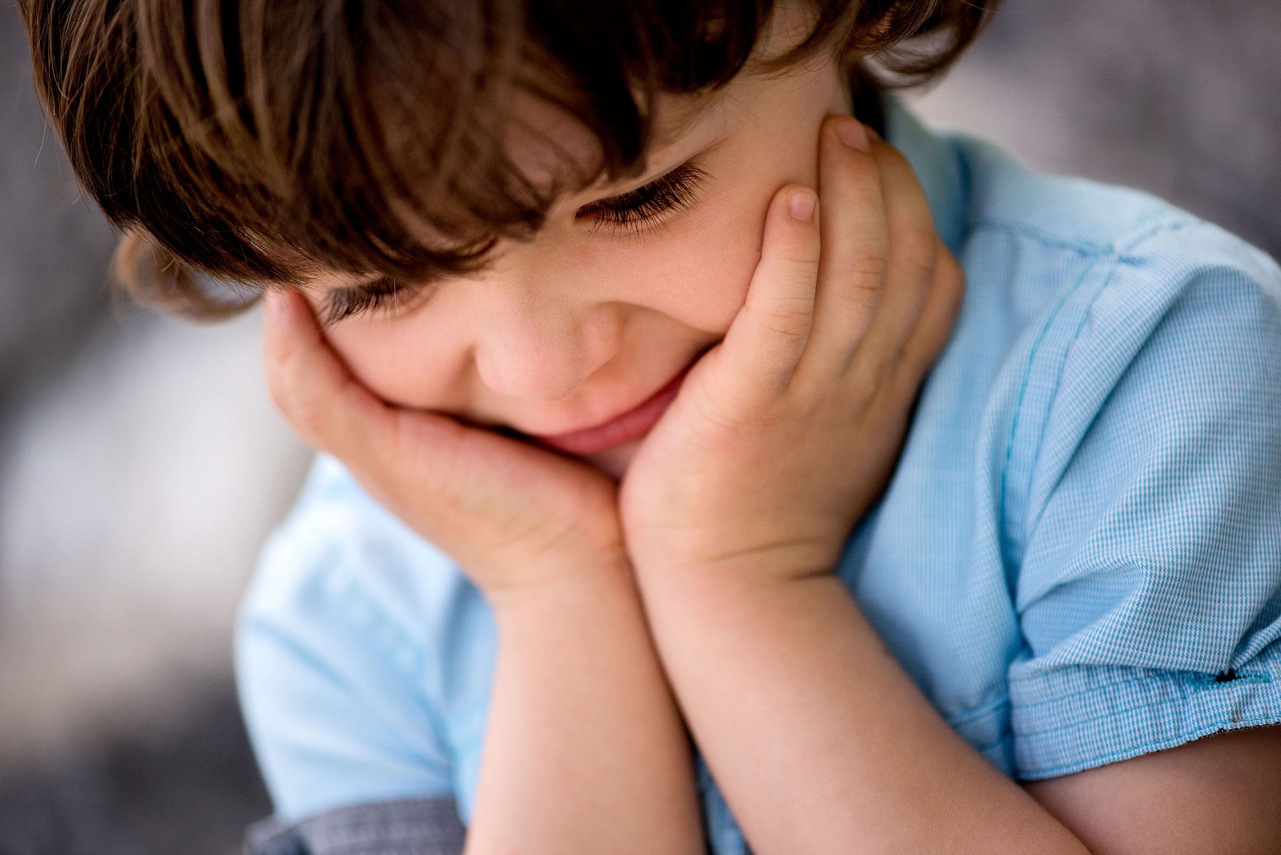 young boy smiling holding his face with his hands by Red Deer Family Photographer Sean LeBlanc