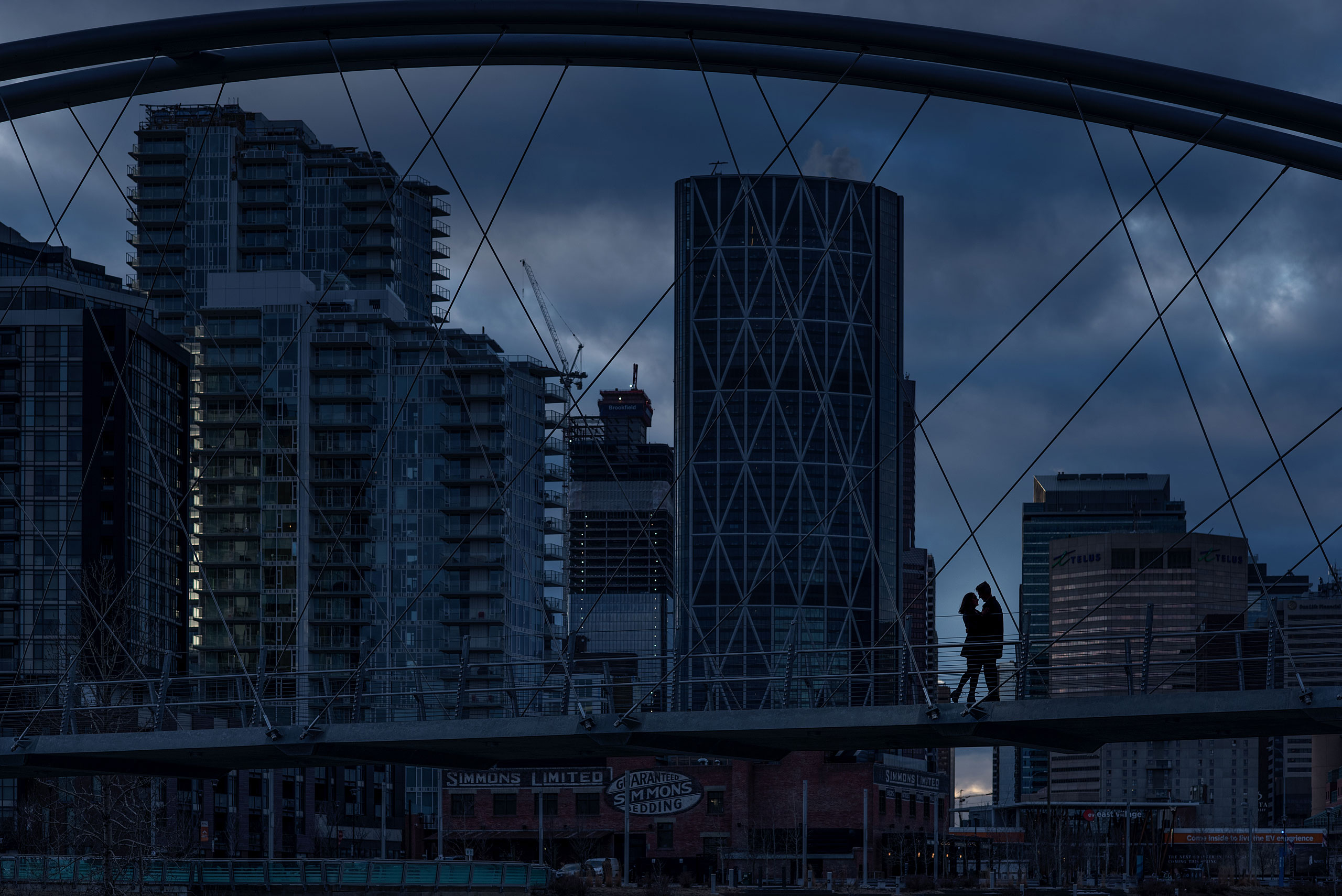 man and women silhouetted on a bridge with a city downtown skyline in the background for Calgary East Village Engagement Session