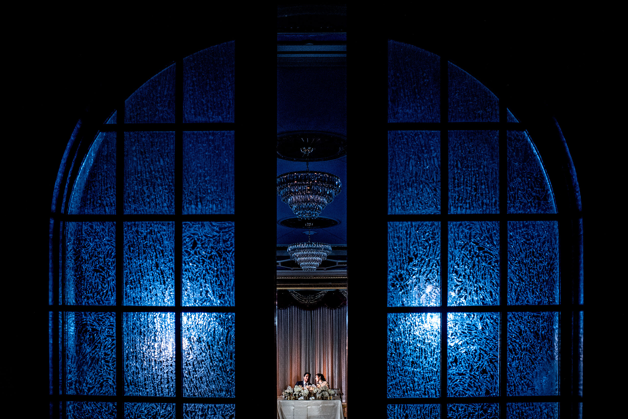 bride and groom sitting at head table in front of doors for cascade ballroom banff springs wedding by sean leblanc