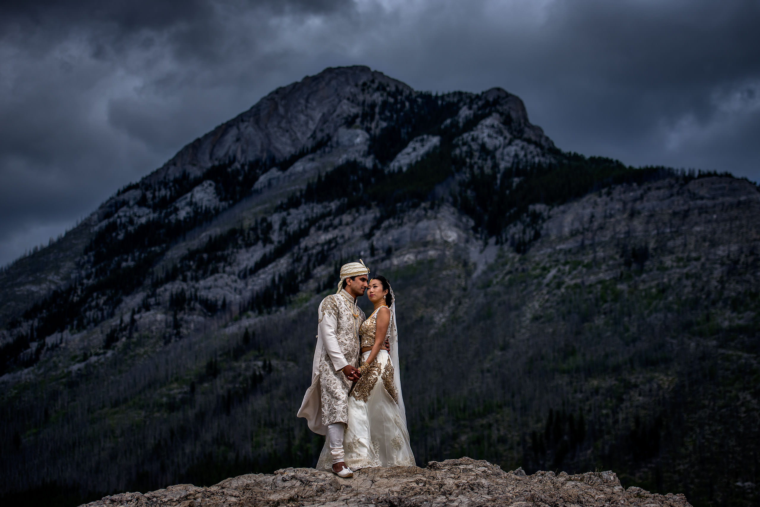 Indian bride and groom wearing traditional Indian wedding clothing embracing on top of a mountain for a cascade ballroom banff springs wedding by sean leblanc