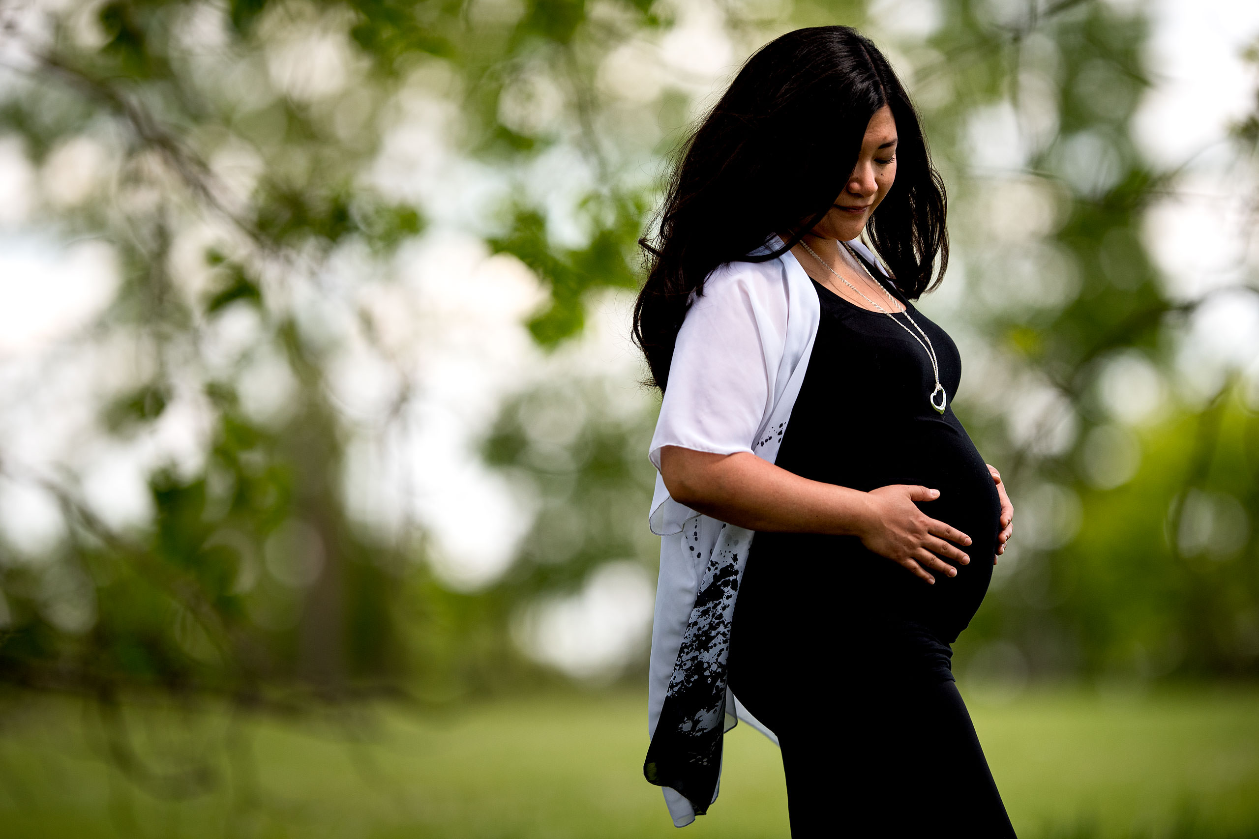 pregnant women wearing a black dress holding her tummy in a natural setting by Calgary Maternity Photographer Sean LeBlanc