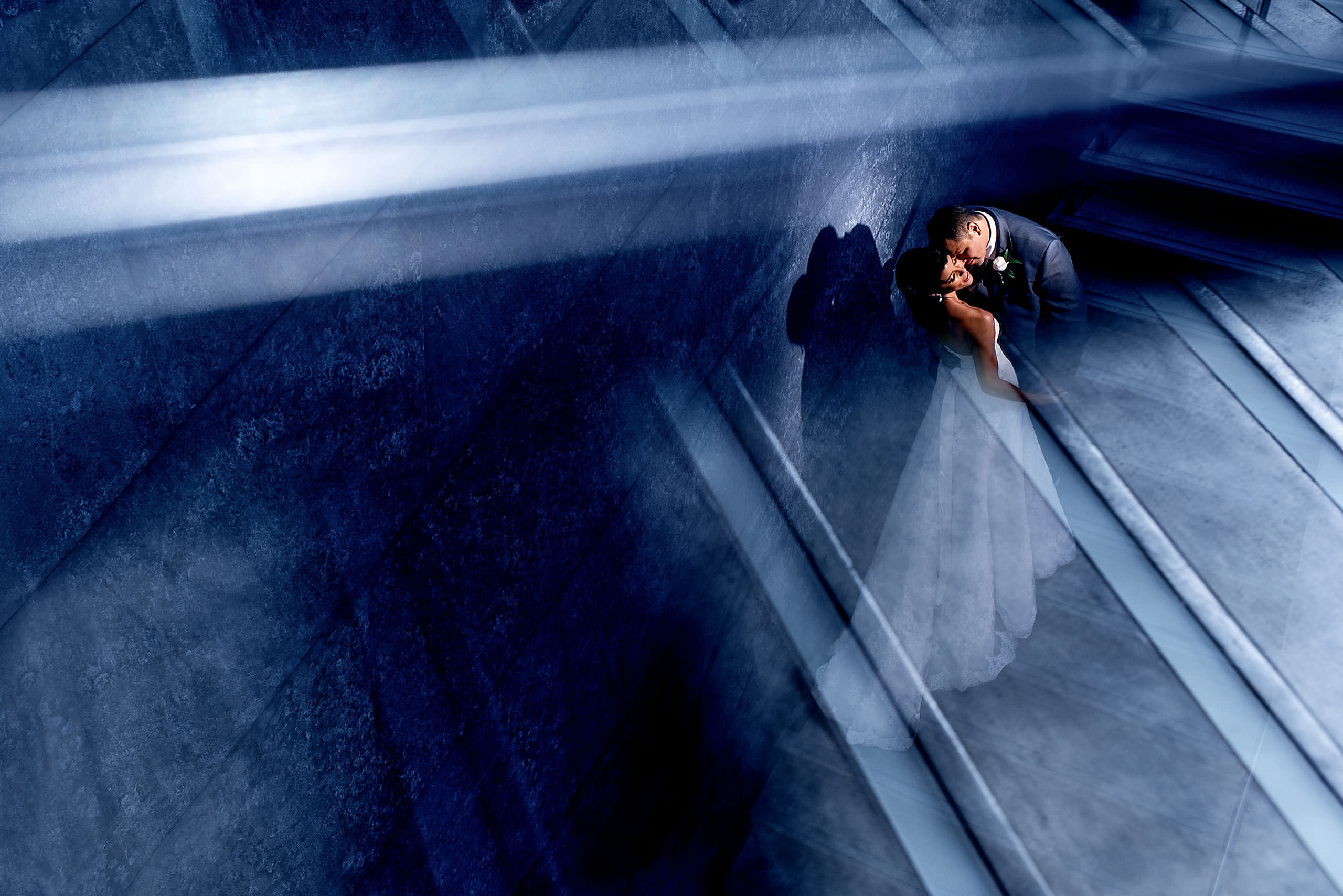 bride and groom embracing on the stairs against a blue backdrop by Edmonton wedding photographer sean leblanc