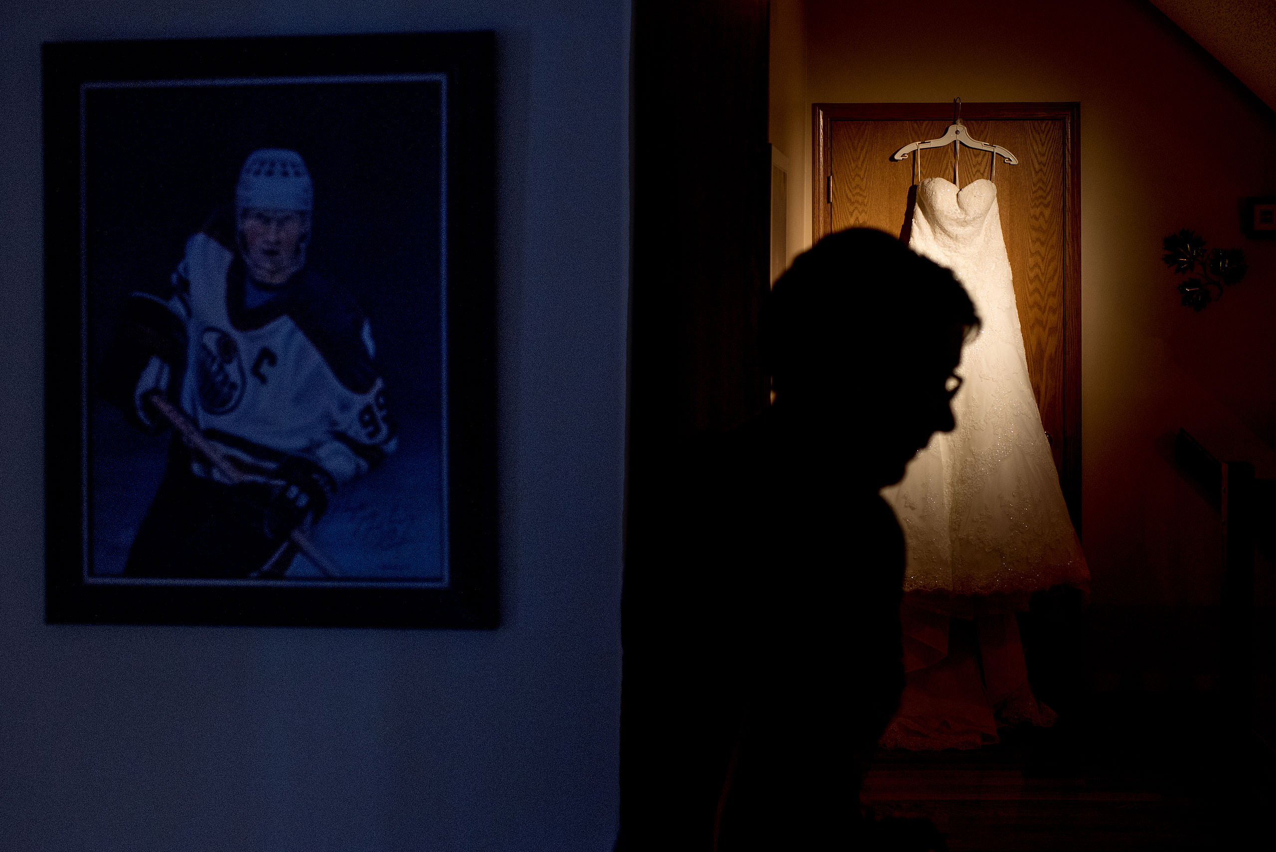 a mother of a bride walks past a wedding dress with Wayne Gretzky photograph hanging on the wall by Edmonton wedding photographer sean leblanc