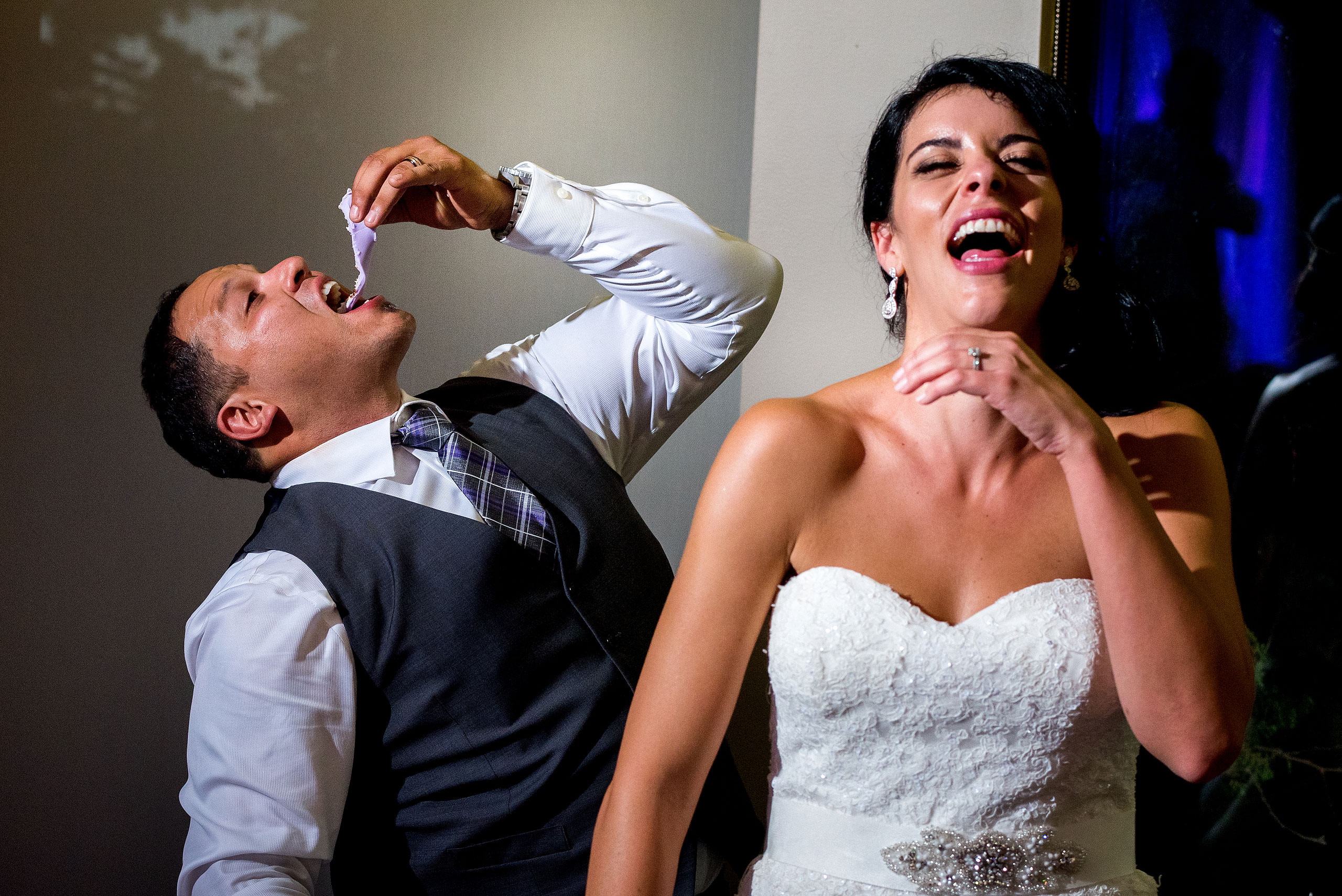 a groom eating a wedding cake with his bride laughing by Edmonton wedding photographer sean leblanc