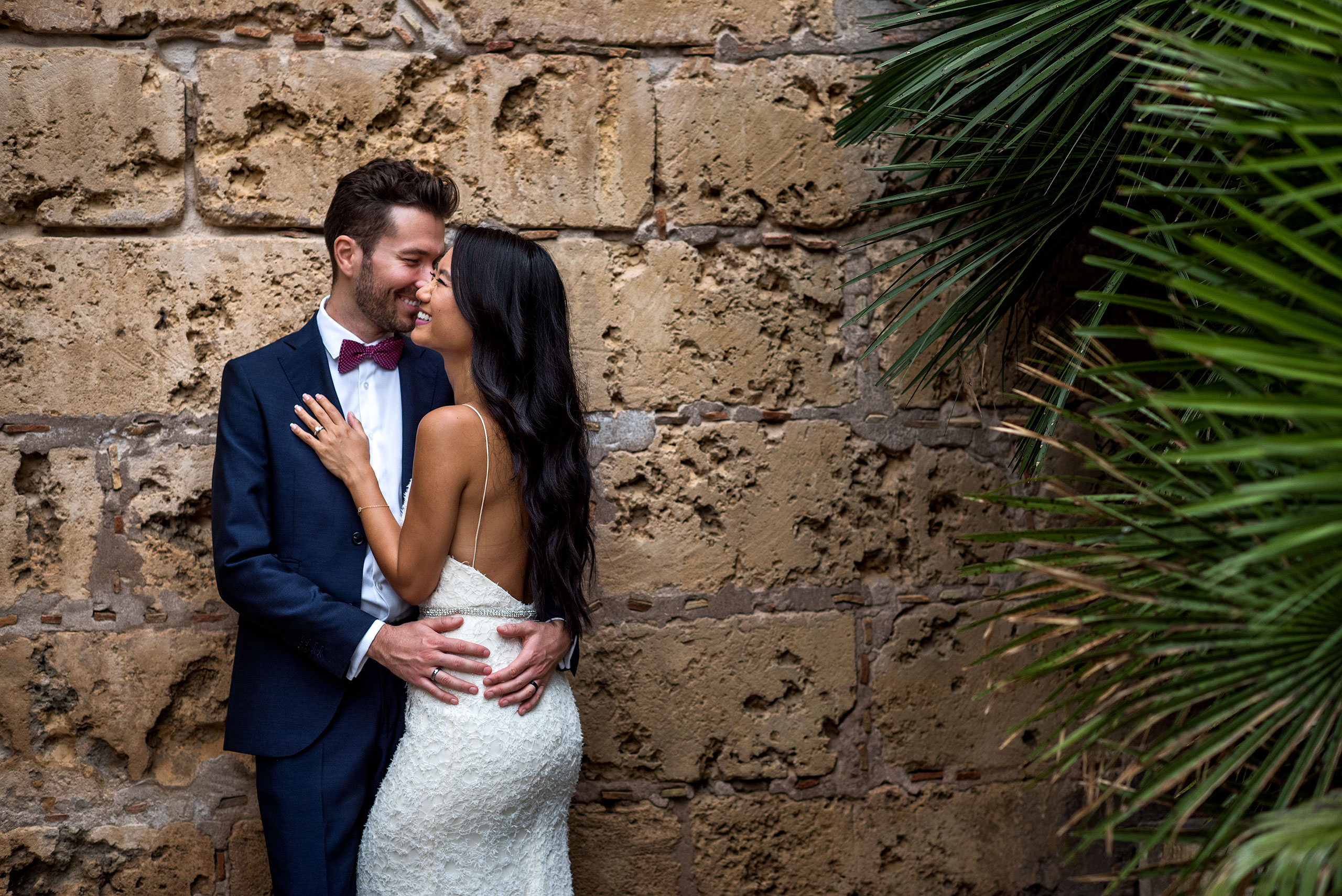 a bride and groom embracing in front of a brick wall at castillo hotel son vida destination wedding by sean leblanc