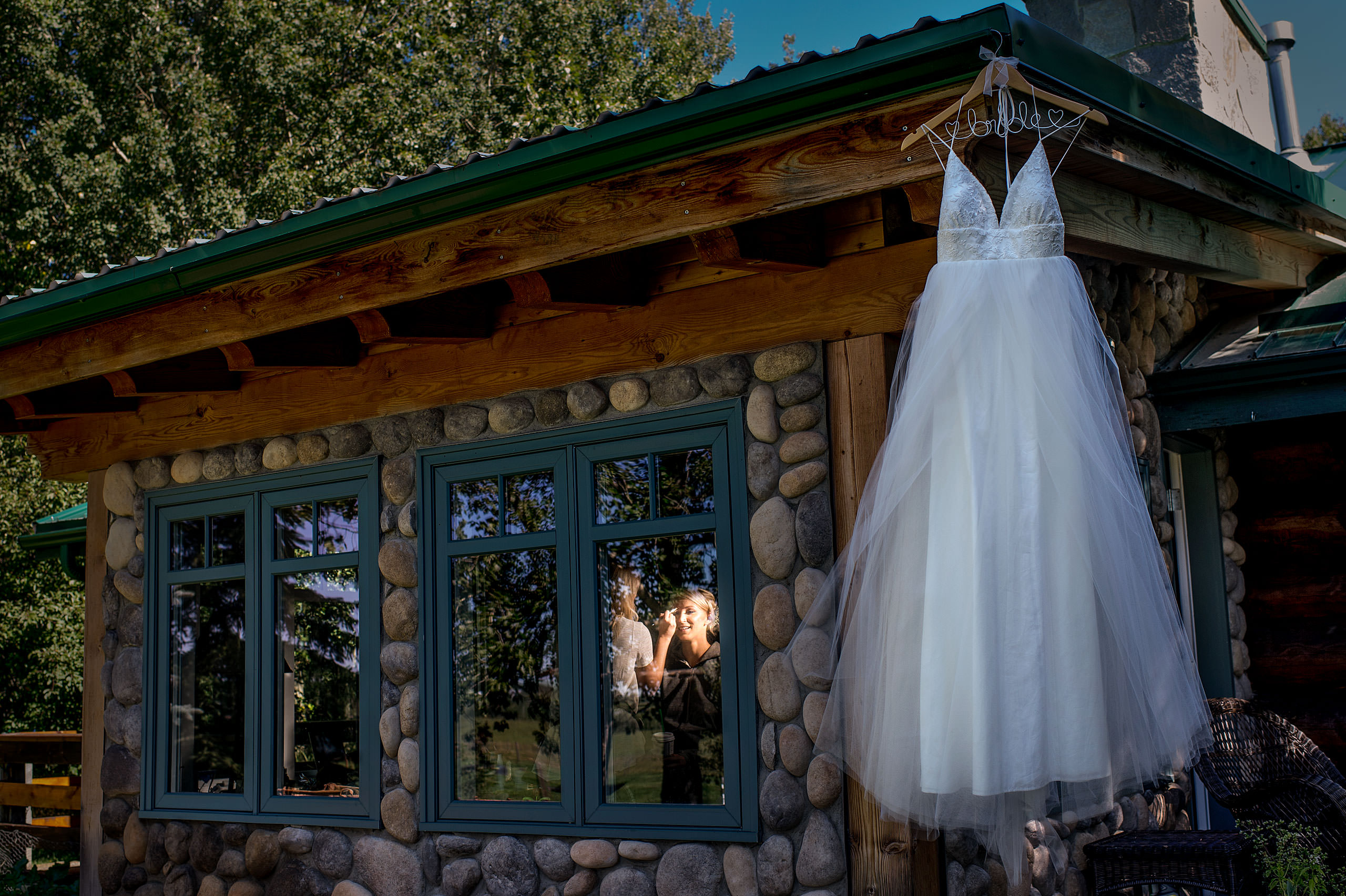 bride getting ready inside of a house with her wedding dress hanging in front at Cochrane Country Wedding by Sean LeBlanc