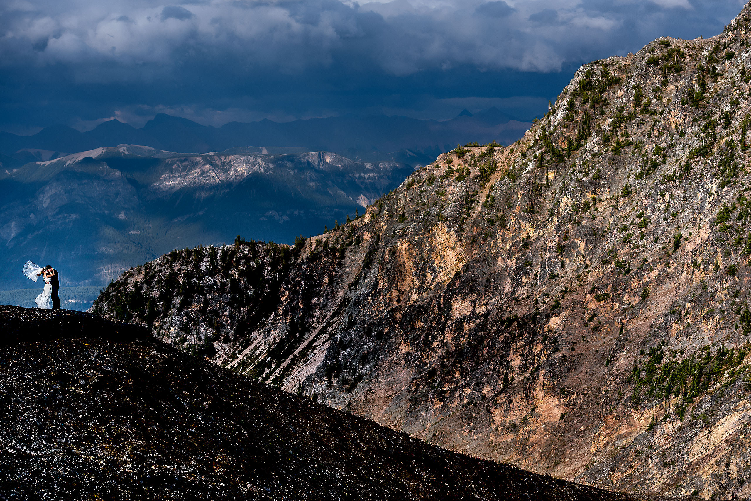 bride and groom embracing on the edge of a mountain with mountains in the background at summer kicking horse wedding