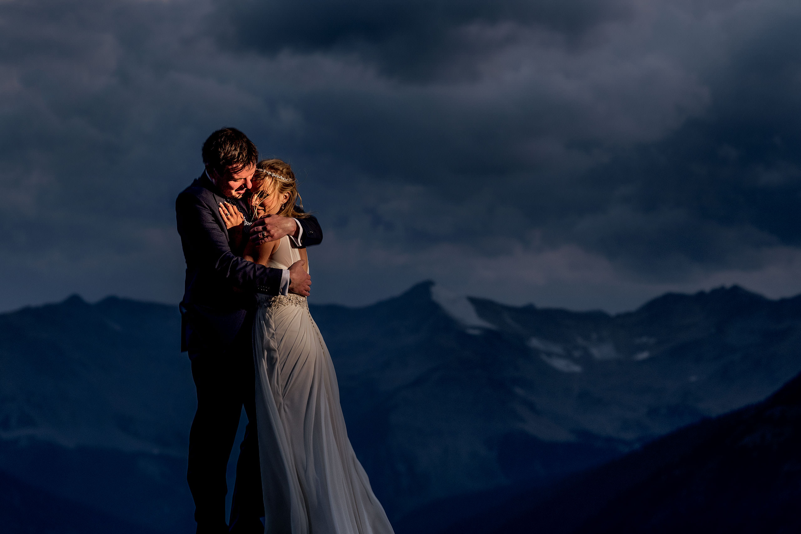 bride and groom embracing on top of a mountain at dusk at summer kicking horse wedding