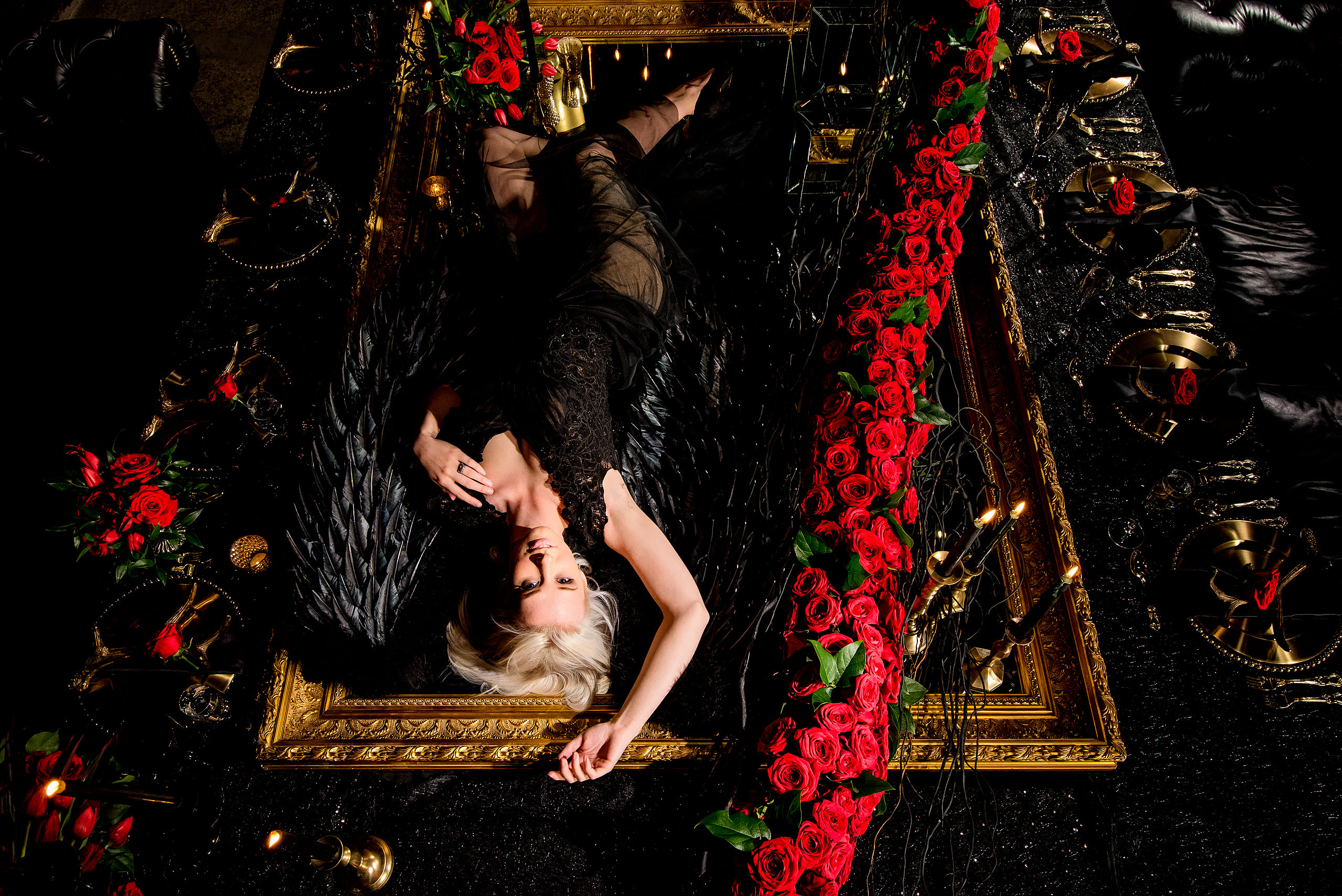 a model wearing a black dress laying down on a mirror beside a string of roses by calgary confetti fashion photographer sean leblanc