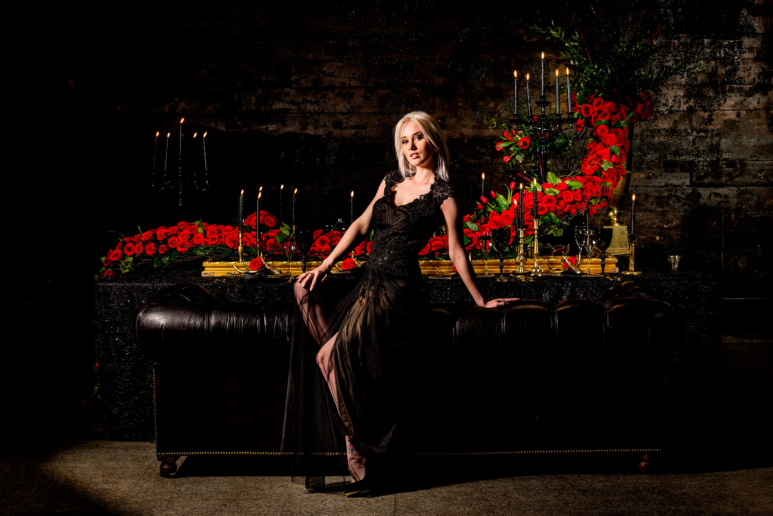 young female model sitting on the edge of a couch in front of a table of roses by calgary confetti fashion photographer sean leblanc