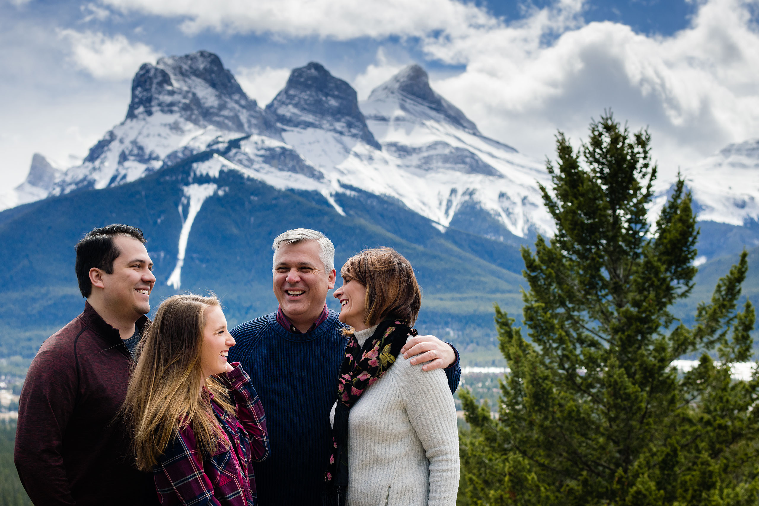 a family of four laughing in front of the three sisters mountains by Canmore Family Photographer Sean LeBlanc