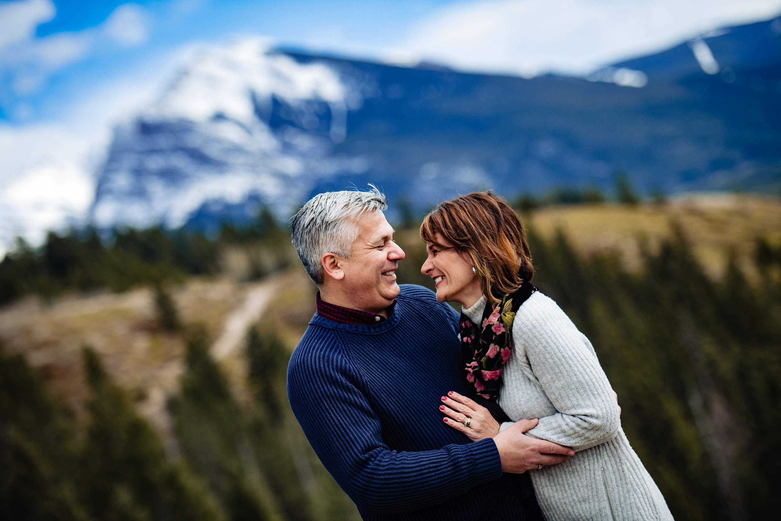 a husband and wife embracing each other with a mountain in the background by Canmore Family Photographer Sean LeBlanc