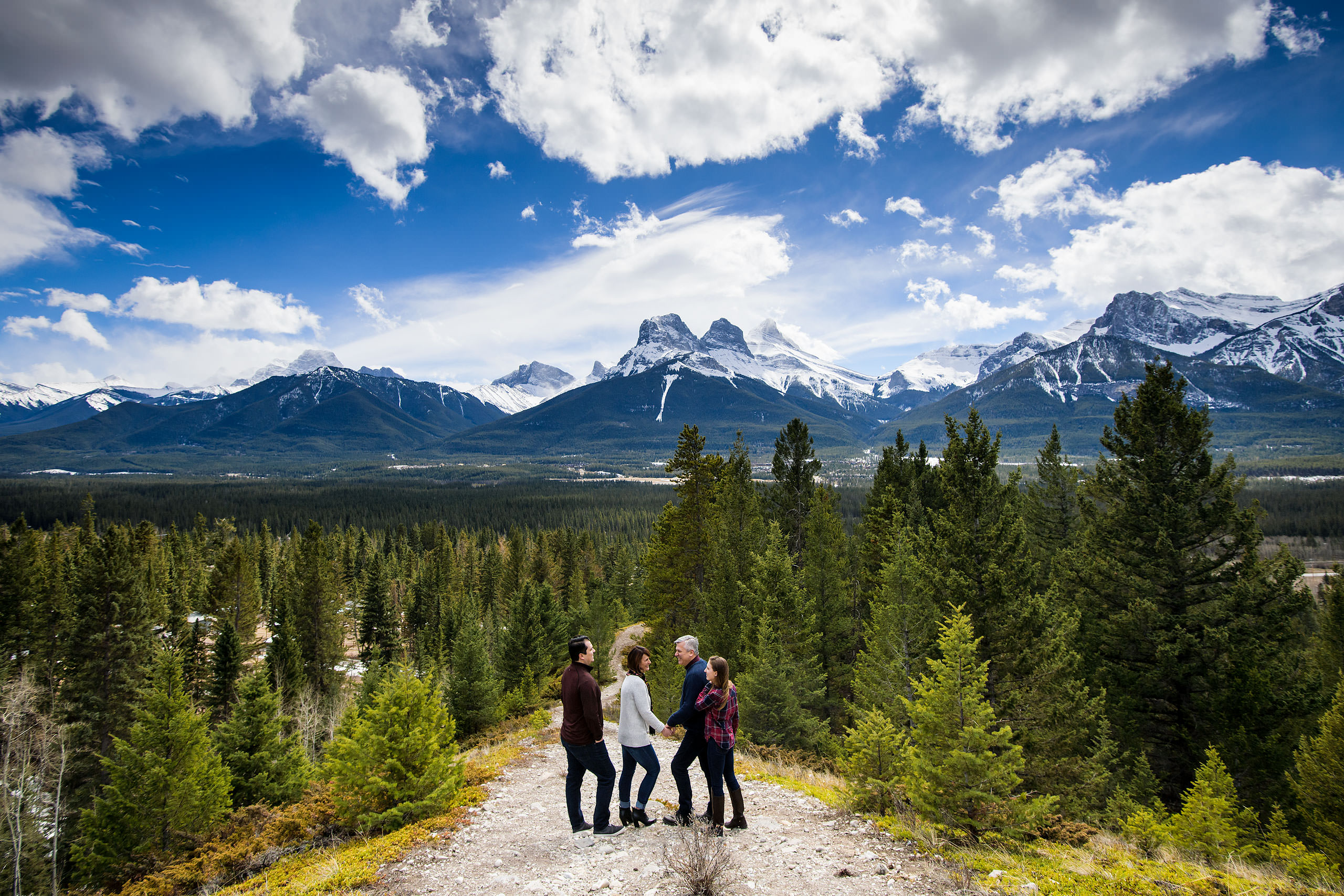 a family of four standing on a pathway smiling at each other by Canmore Family Photographer Sean LeBlanc