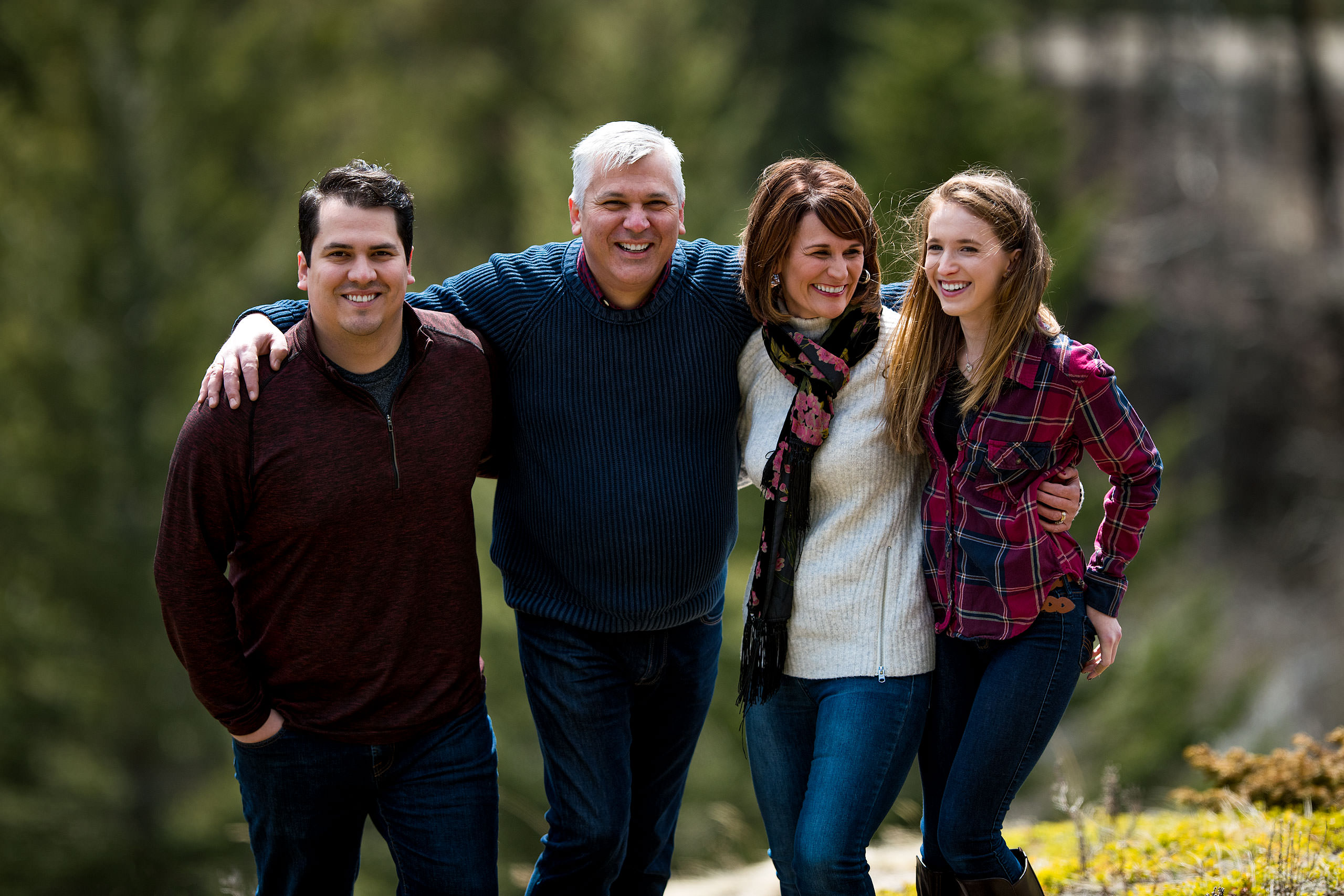 a family of four with their arms around each other smiling by Canmore Family Photographer Sean LeBlanc