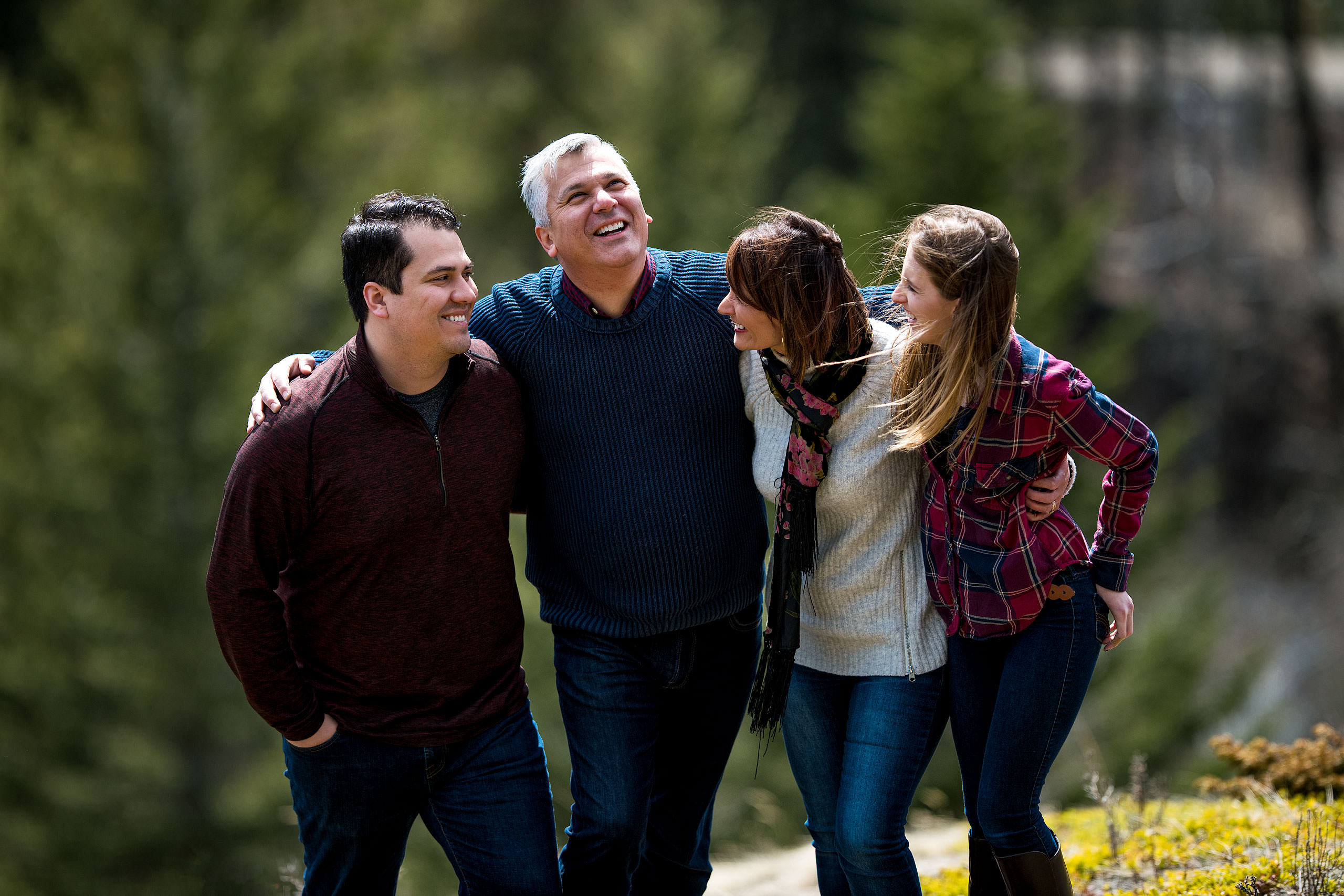 a family of four with their arms around each other laughing by Canmore Family Photographer Sean LeBlanc