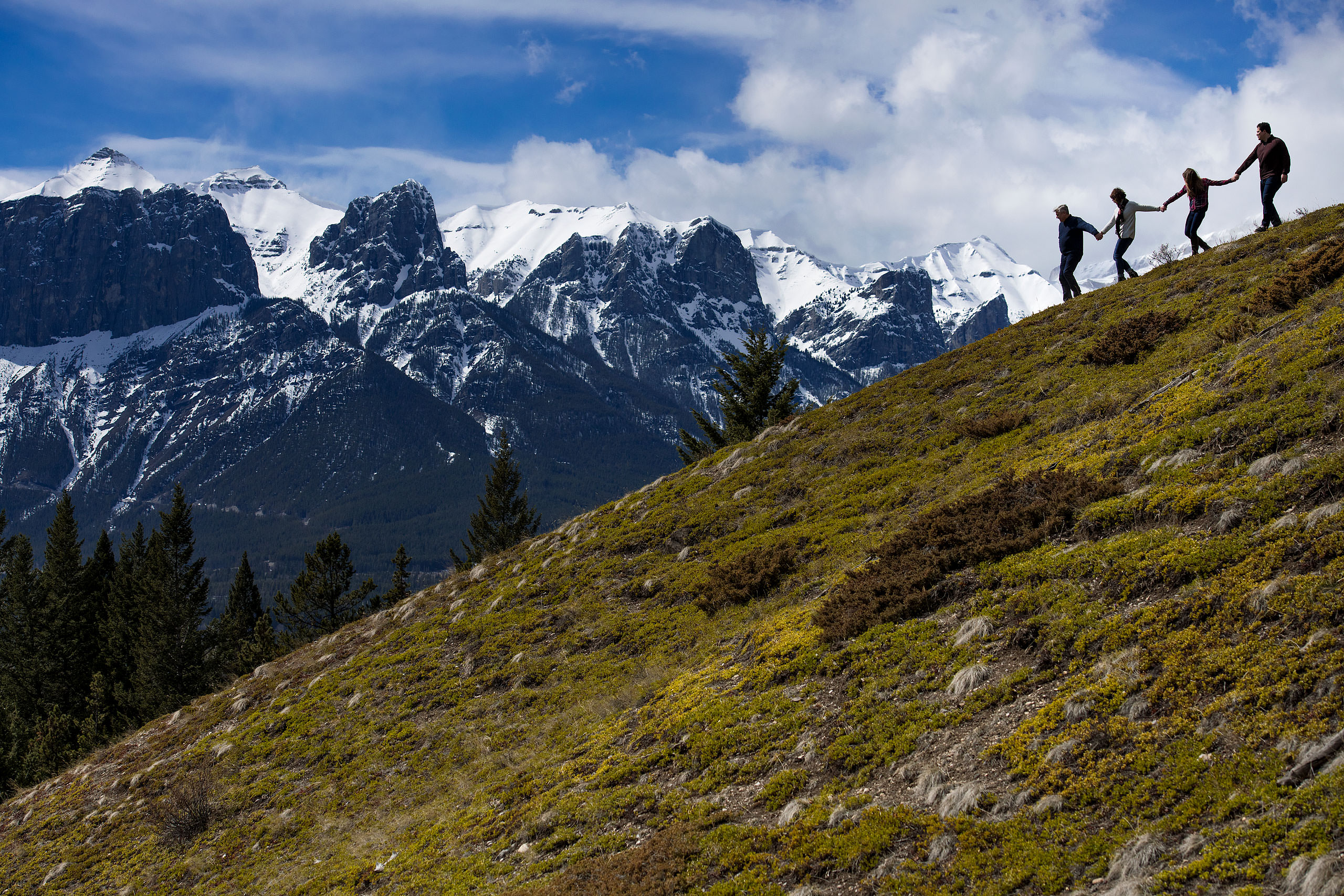 a family of four holding hands walking down a mountain by Canmore Family Photographer Sean LeBlanc