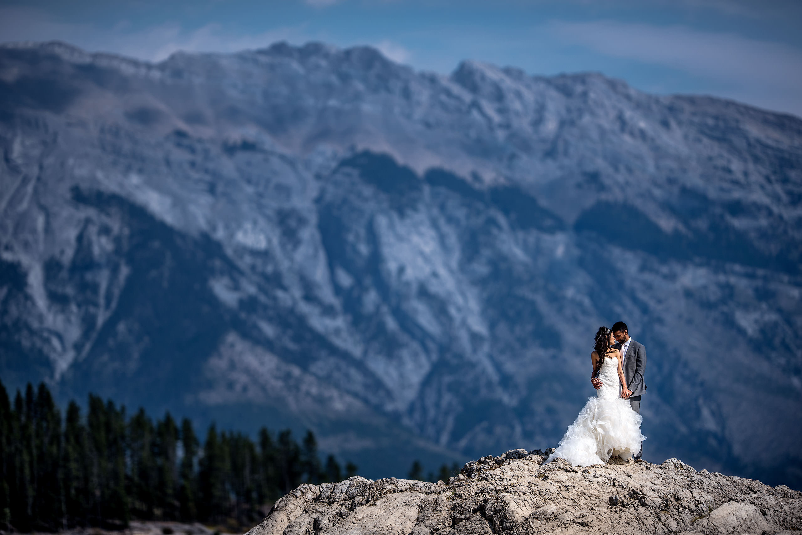 a bride and groom embracing on top of a rock with a mountain in the background by Calgary Banff Wedding Photographer Sean LeBlanc