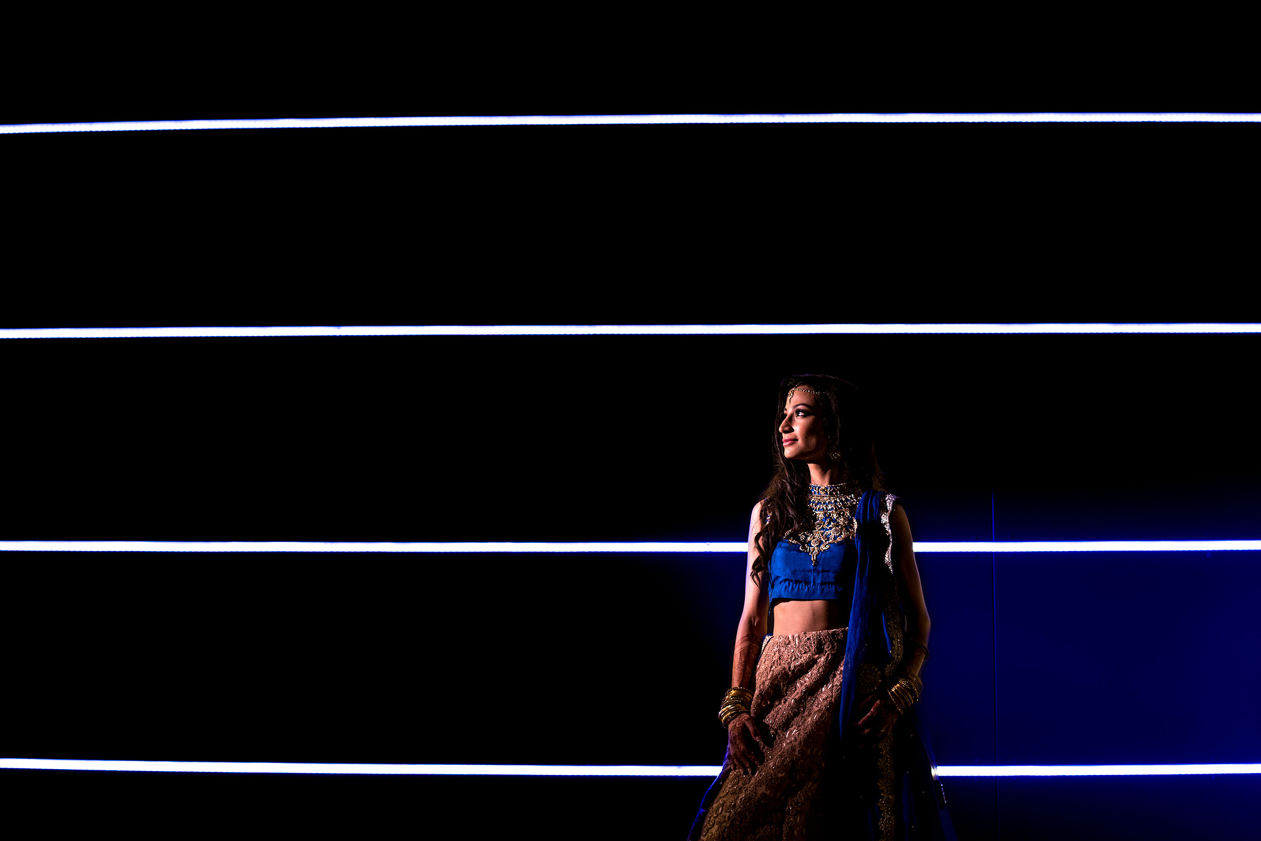 an indian bride wearing a blue dress standing in front of lines on a wall by Calgary Banff Wedding Photographer Sean LeBlanc