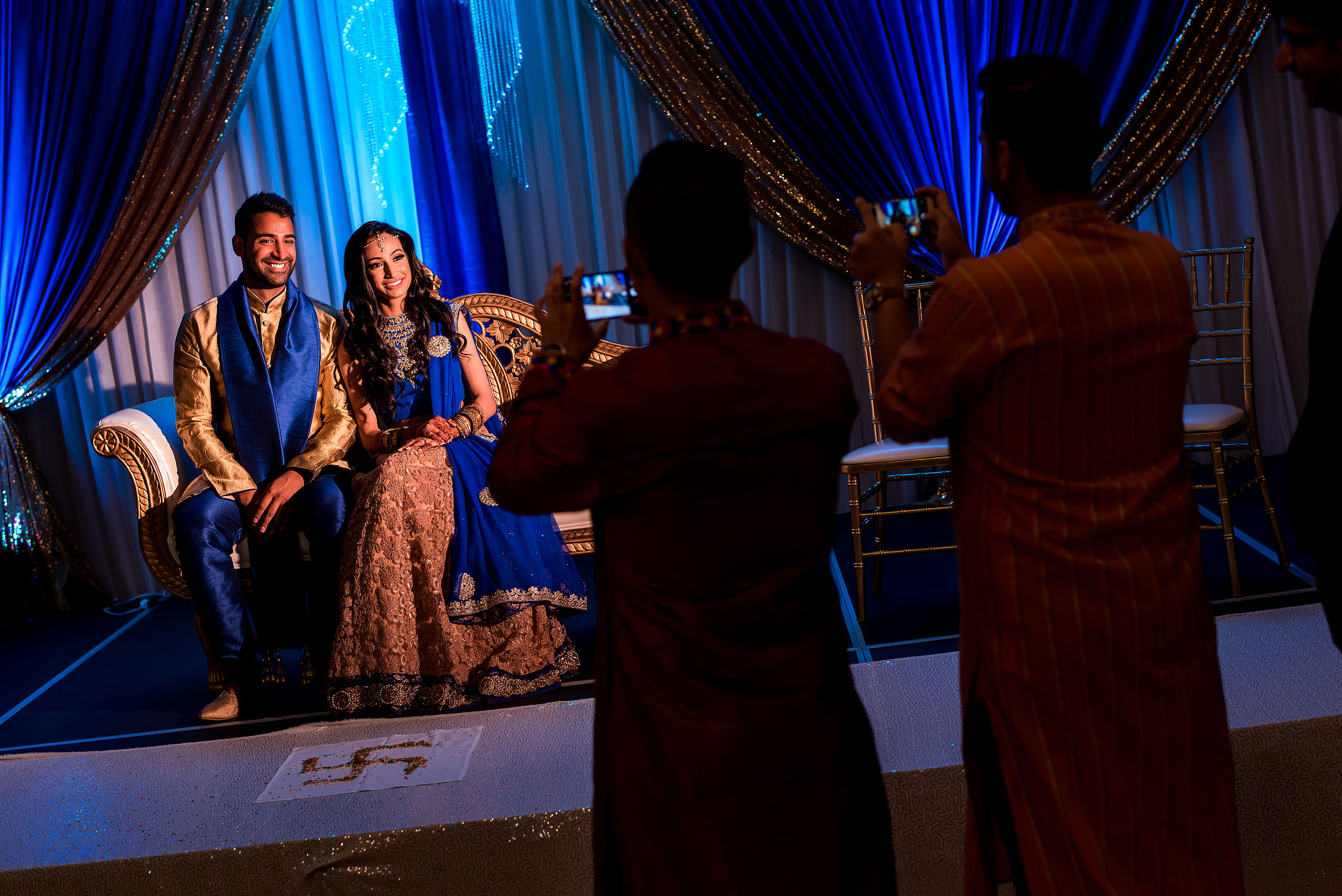 an indian bride and groom sitting on chairs having their photo taken by wedding guests by Calgary Banff Wedding Photographer Sean LeBlanc