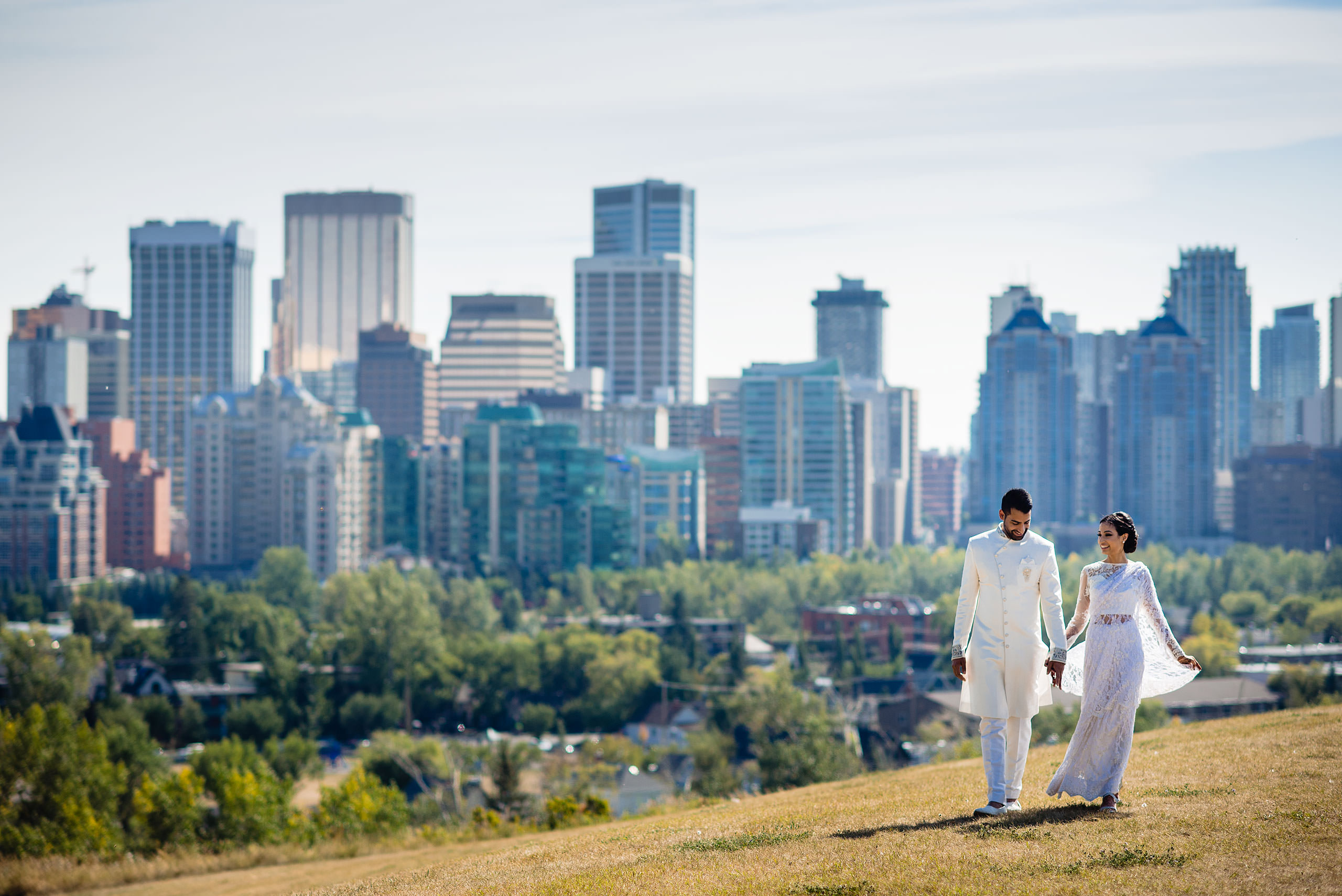 an Indian bride and groom walking on a hill in front of downtown Calgary by Calgary Banff Wedding Photographer Sean LeBlanc