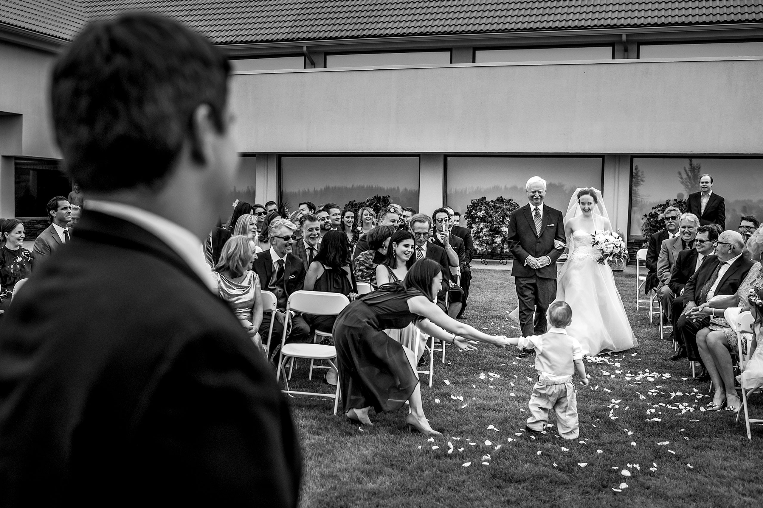 a bride and her dad walking down the aisle at a wedding ceremony and a little boy stopped in the aisle by award winning photographer sean leblanc