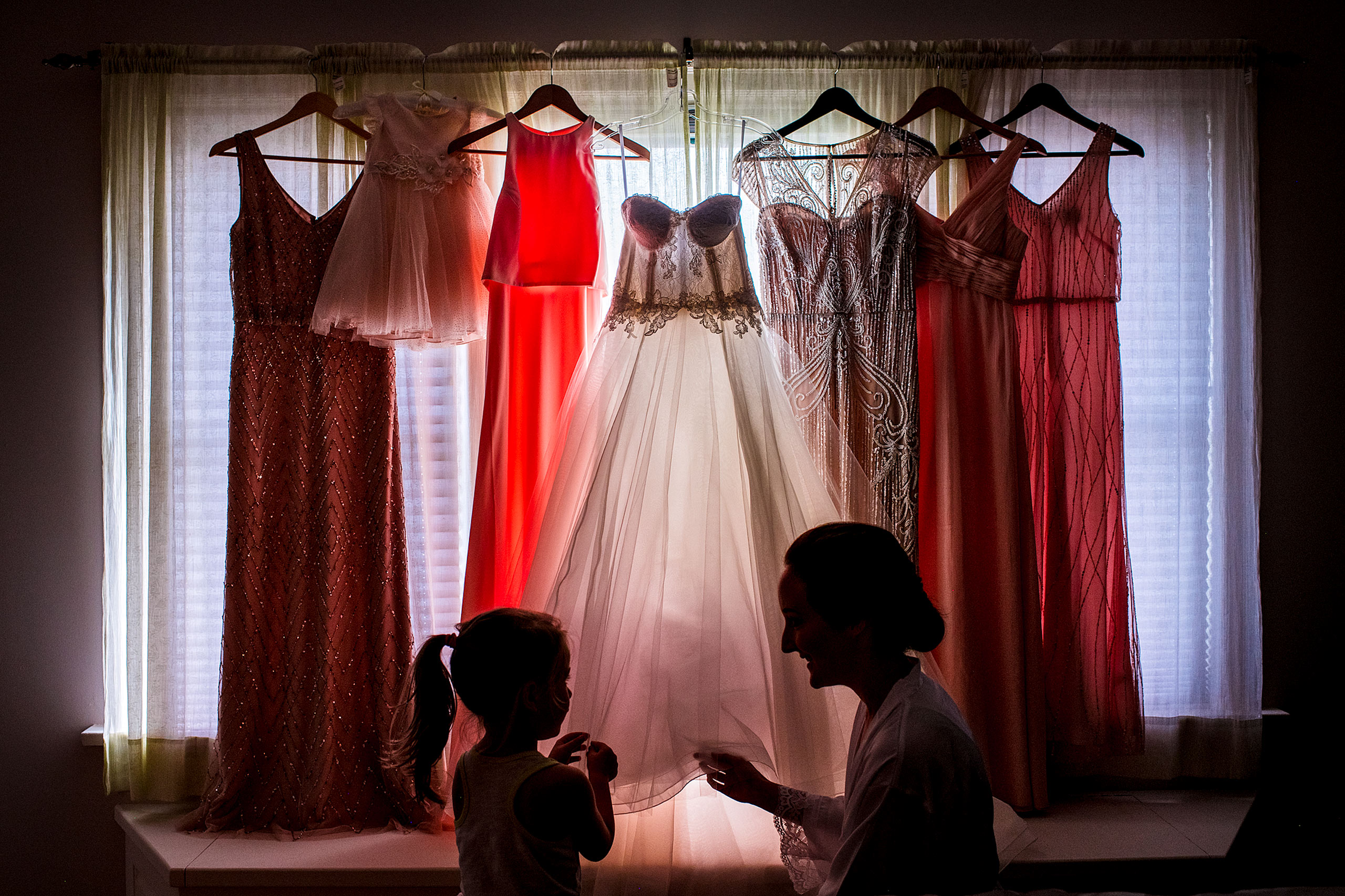 a bride showing a flower girl her wedding dress in front of a window by calgary wedding photographer sean leblanc