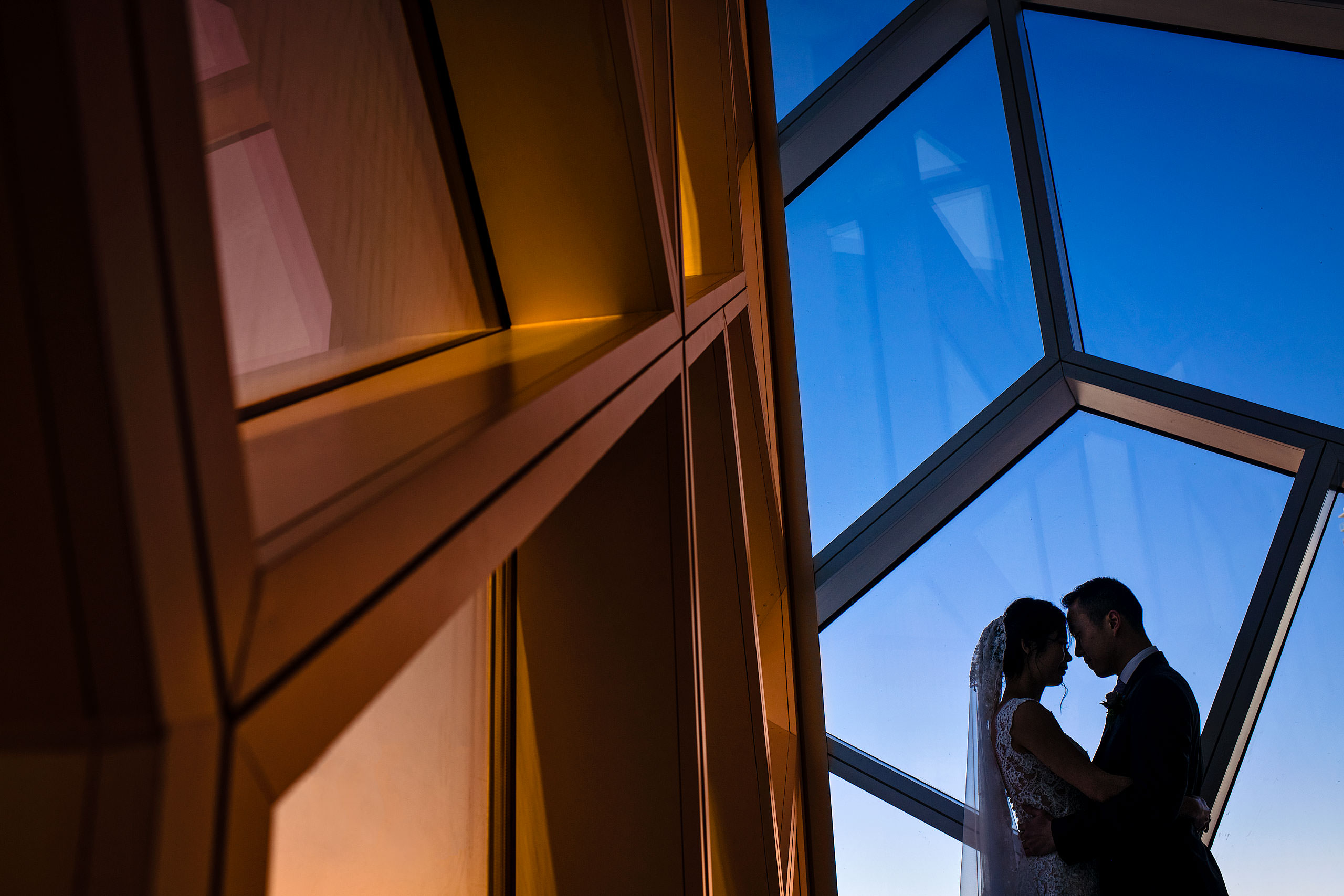 a bride and groom standing by a window at the calgary library for their calgary lake house wedding by calgary wedding photographer sean leblanc photography