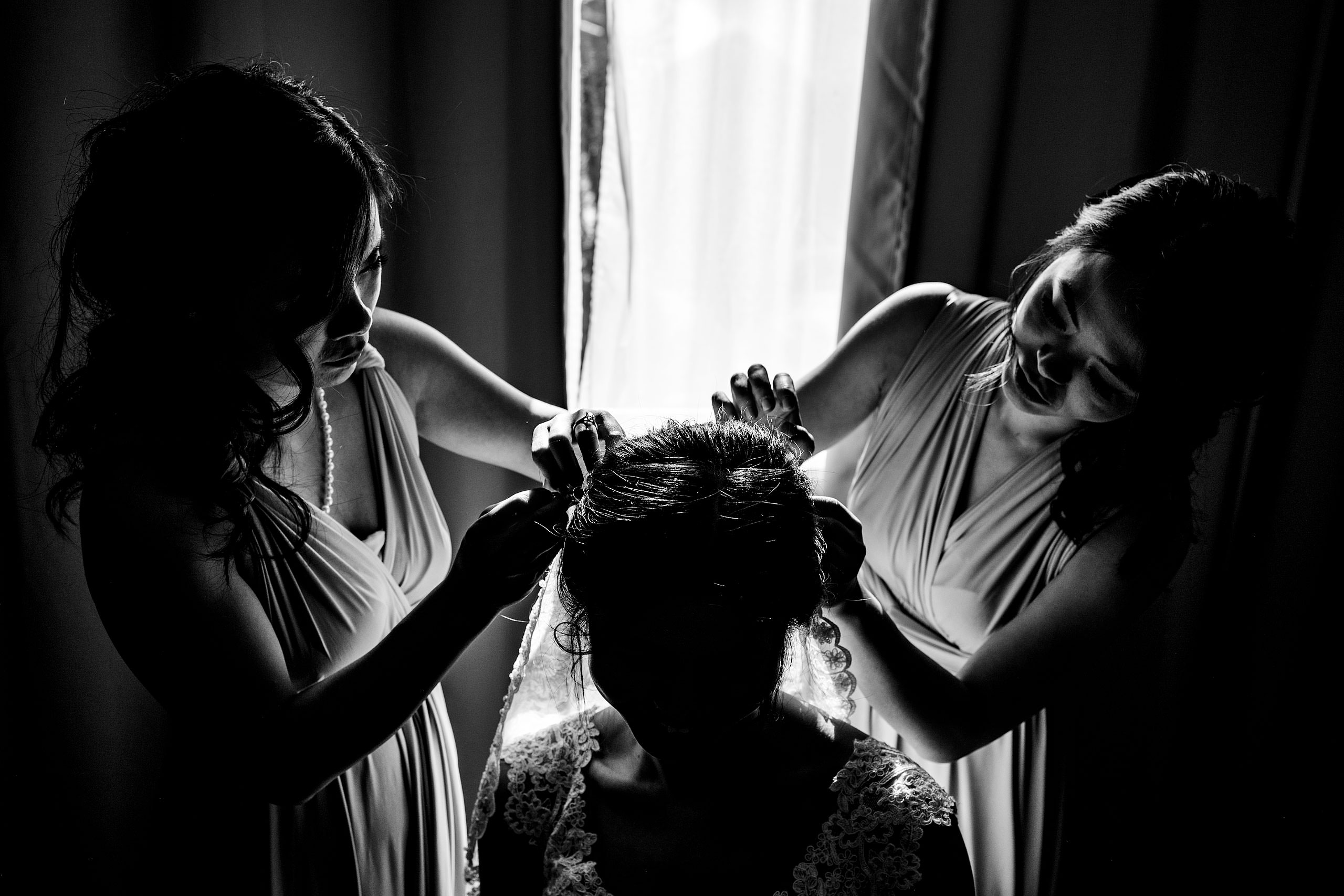 two bridesmaids helping a bride put on her veil at a calgary lake house wedding by calgary wedding photographer sean leblanc photography