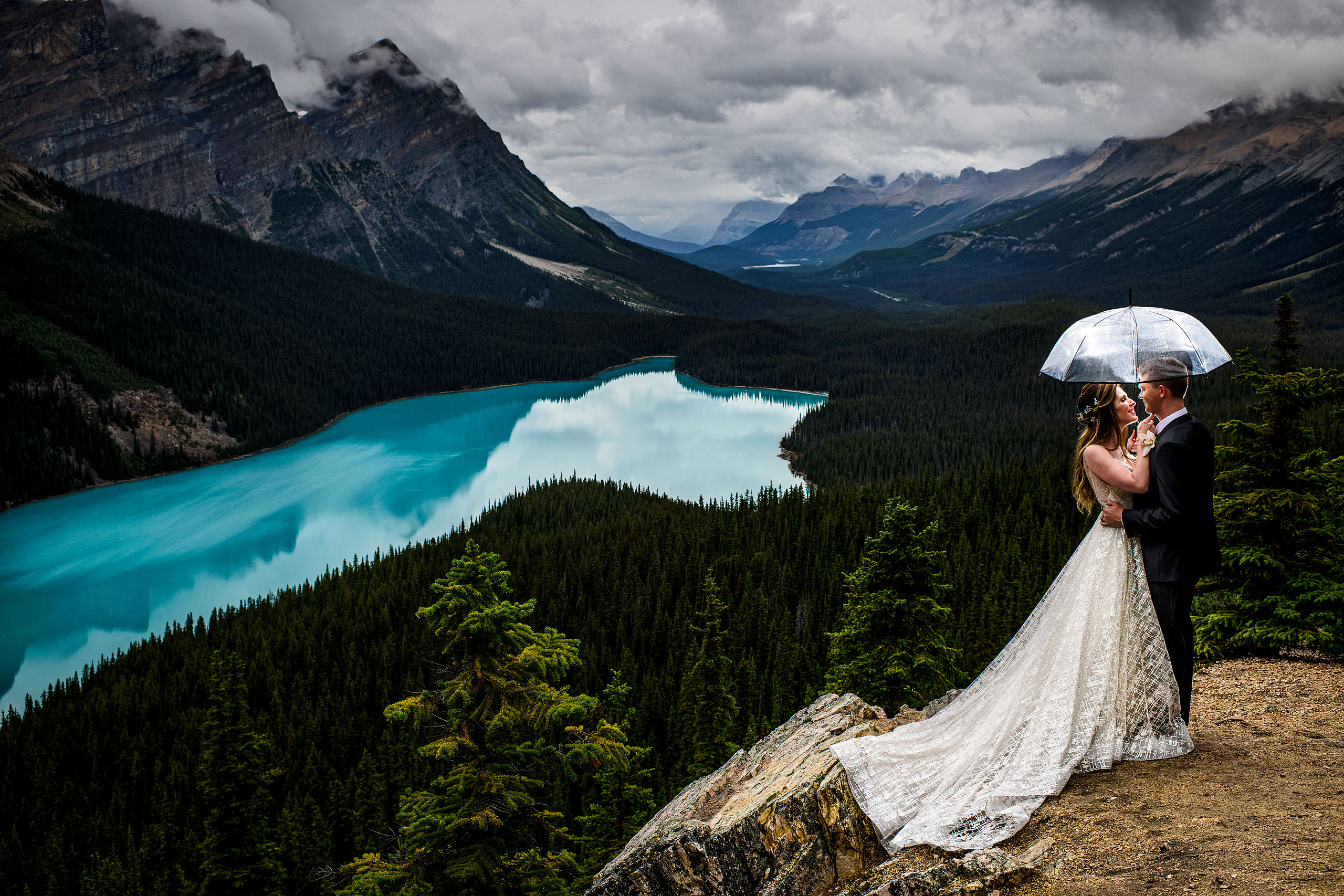 Bride and groom standing under an umbrella looking at each other by Peyto Lake by lake louise wedding photographer sean leblanc