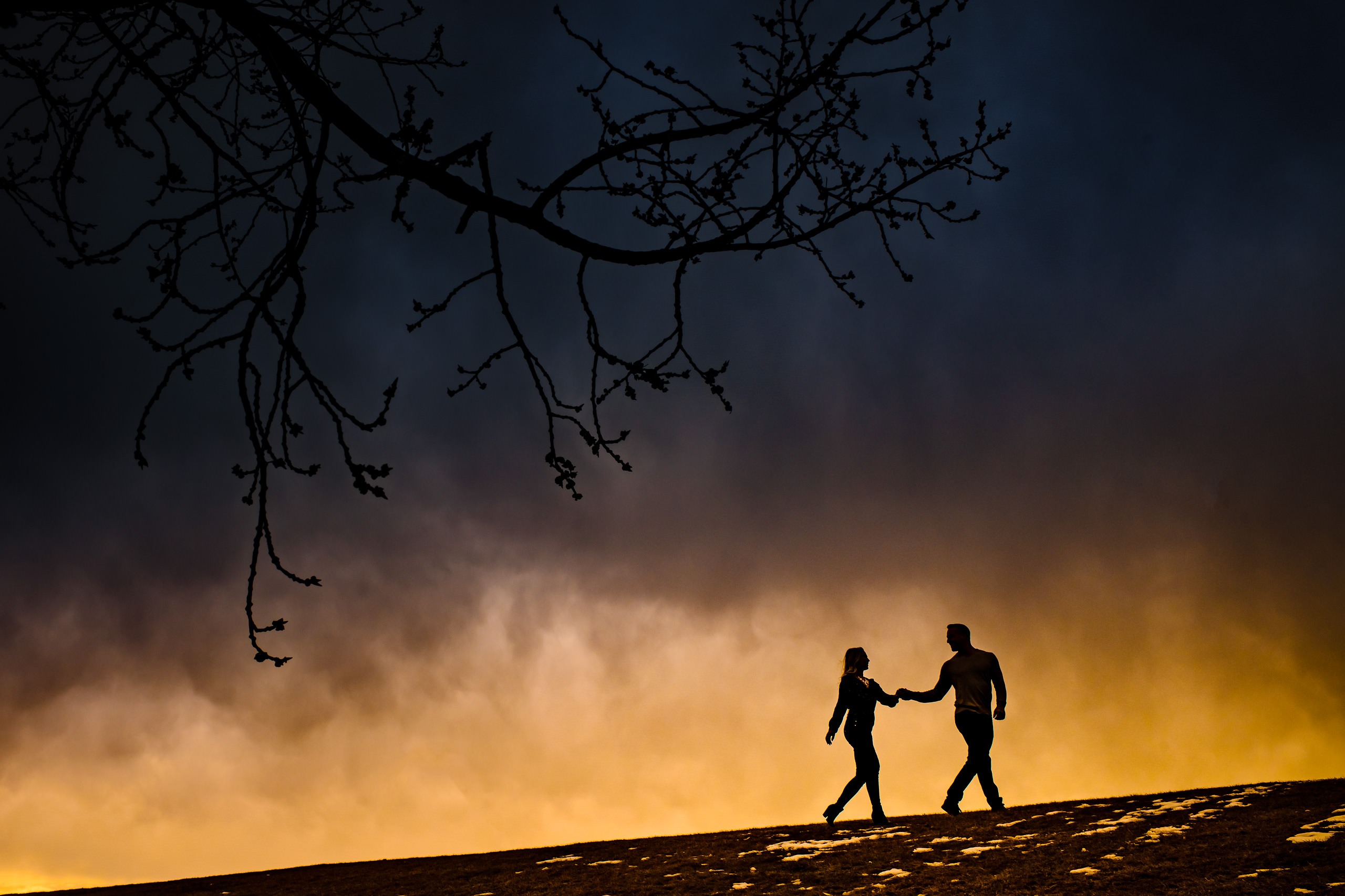 Man and a women walking along a hill top at sunset by calgary engagement photographer sean leblanc